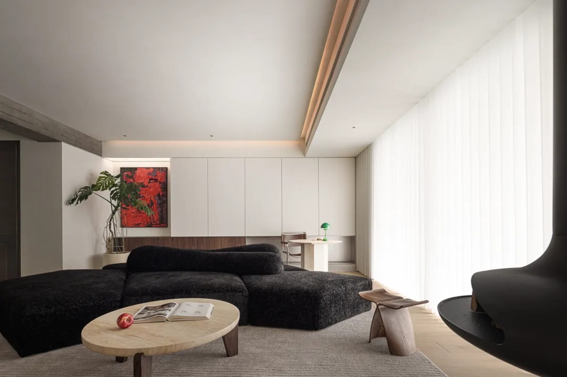 A minimalist living room with a black upholstered sofa, a wooden coffee table, white cabinetry, and glass panel drapes.