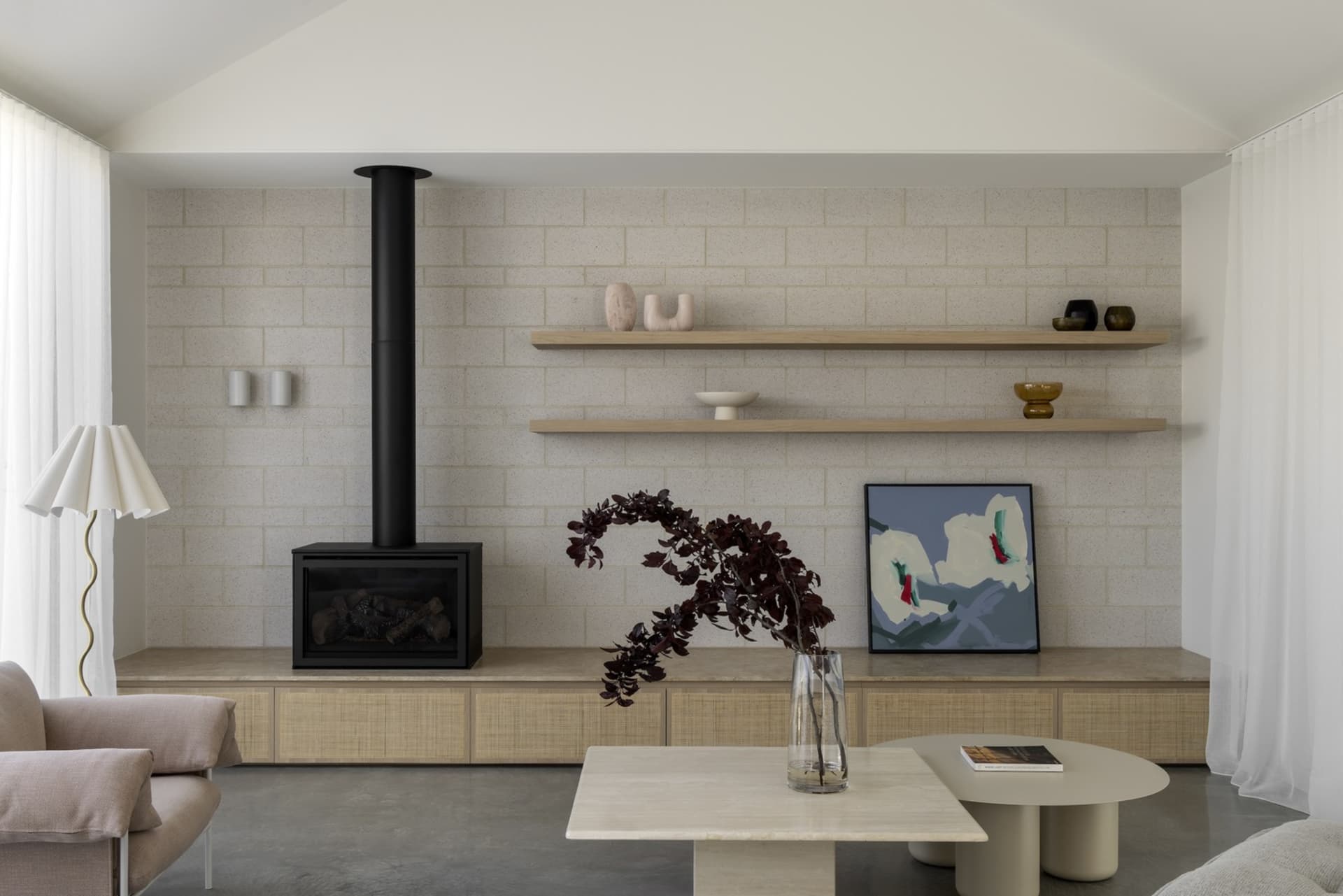 Modern living room with cement brick accent wall, floating shelves, and minimalistic furniture.