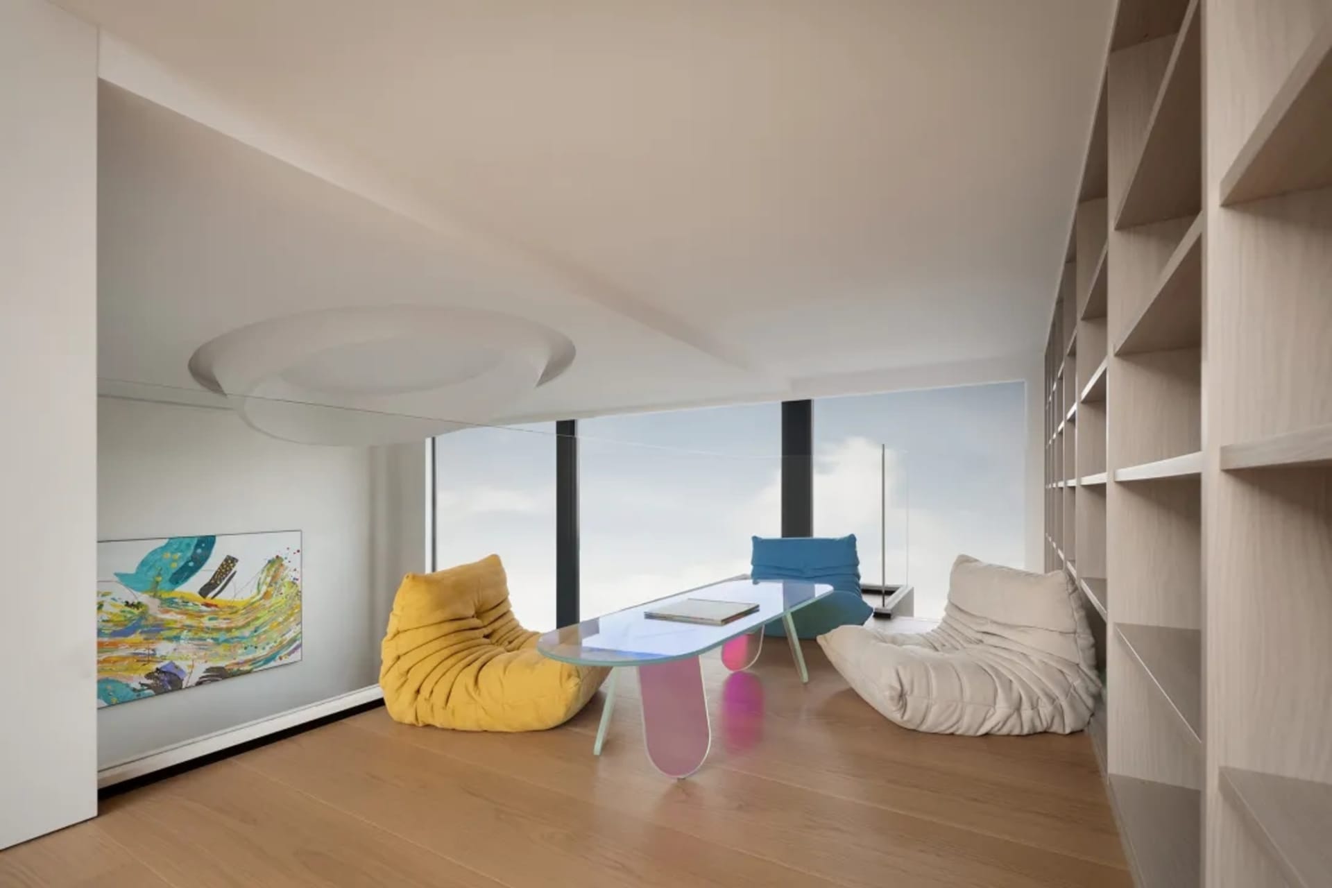 Modern living room with wood flooring, glass coffee table, and colorful sofas.