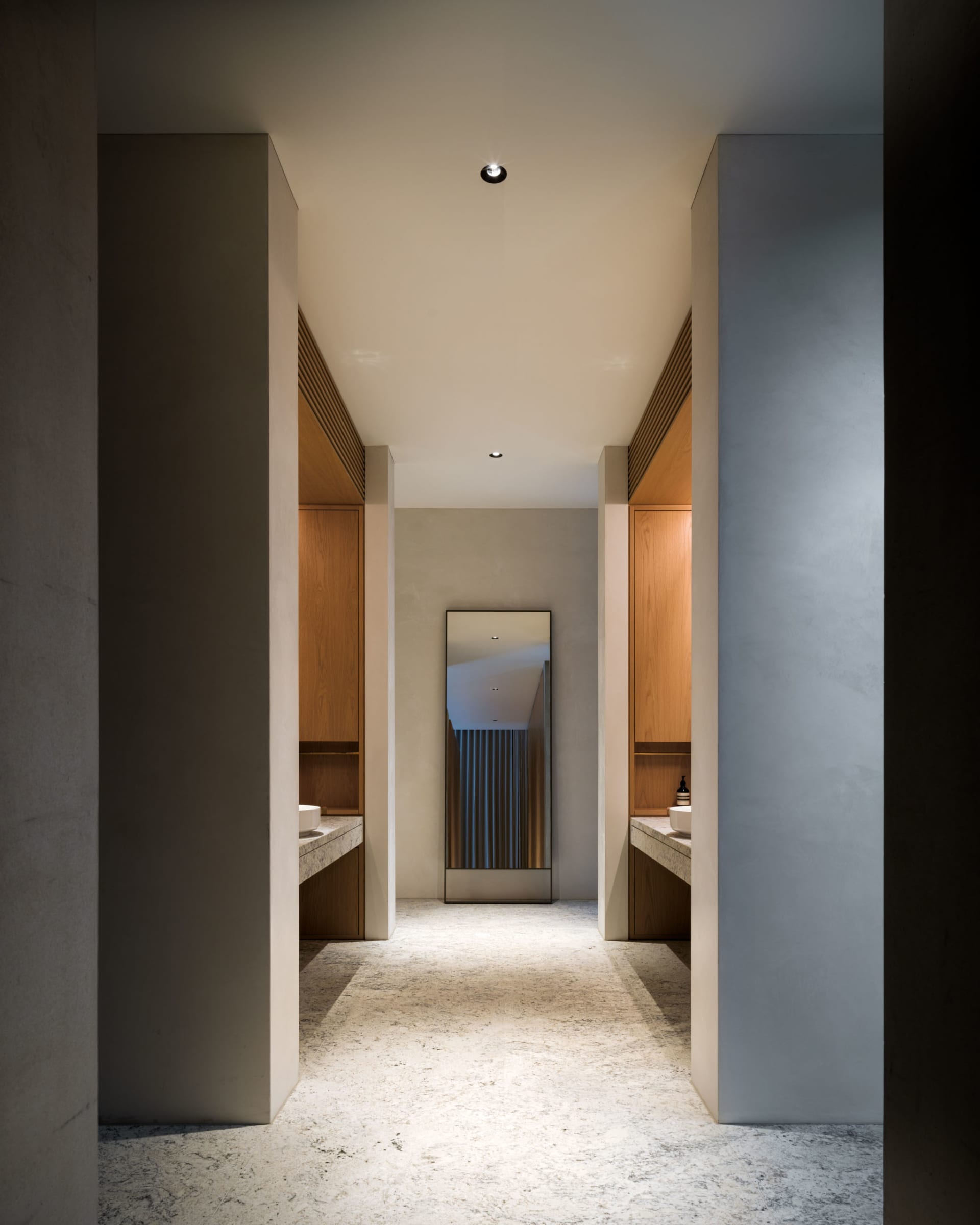 A minimalist bathroom with concrete flooring, wooden cabinets, and a large mirror.