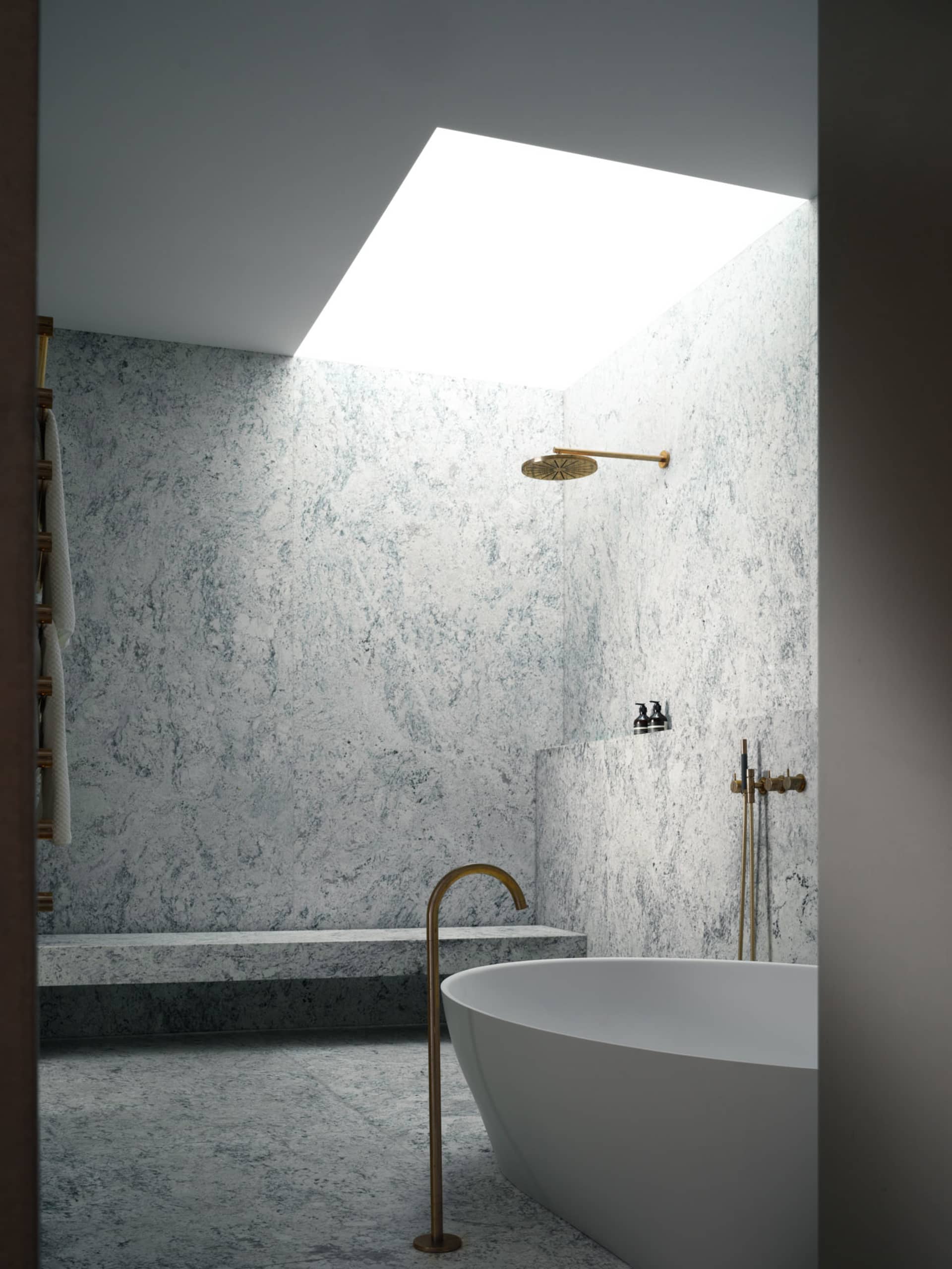 A modern bathroom featuring a freestanding bathtub with a sleek design, marble walls, and a granite floor under a skylight.