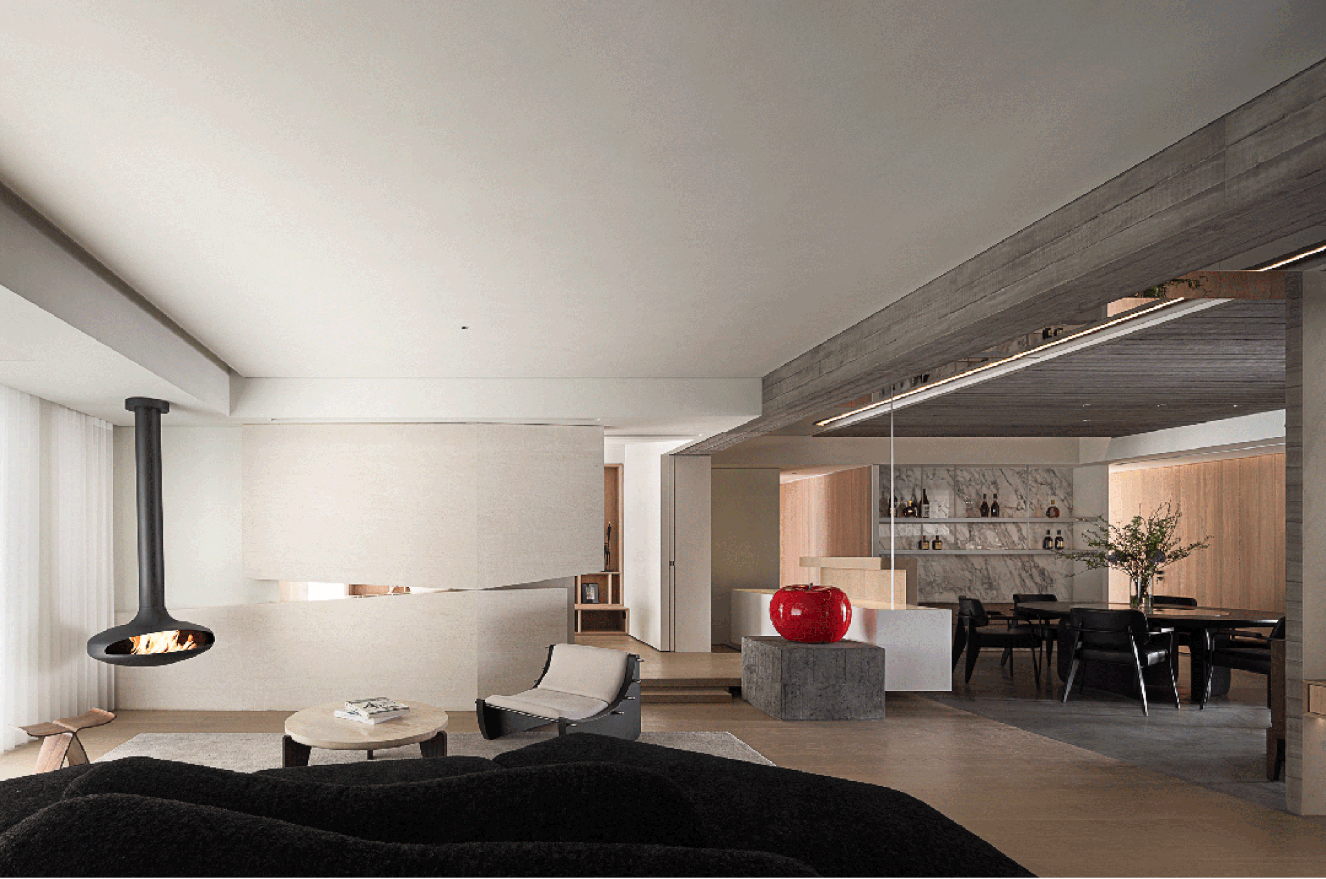 Modern living room with concrete fireplace, minimalist furniture, and red decorative apple on concrete pedestal.
