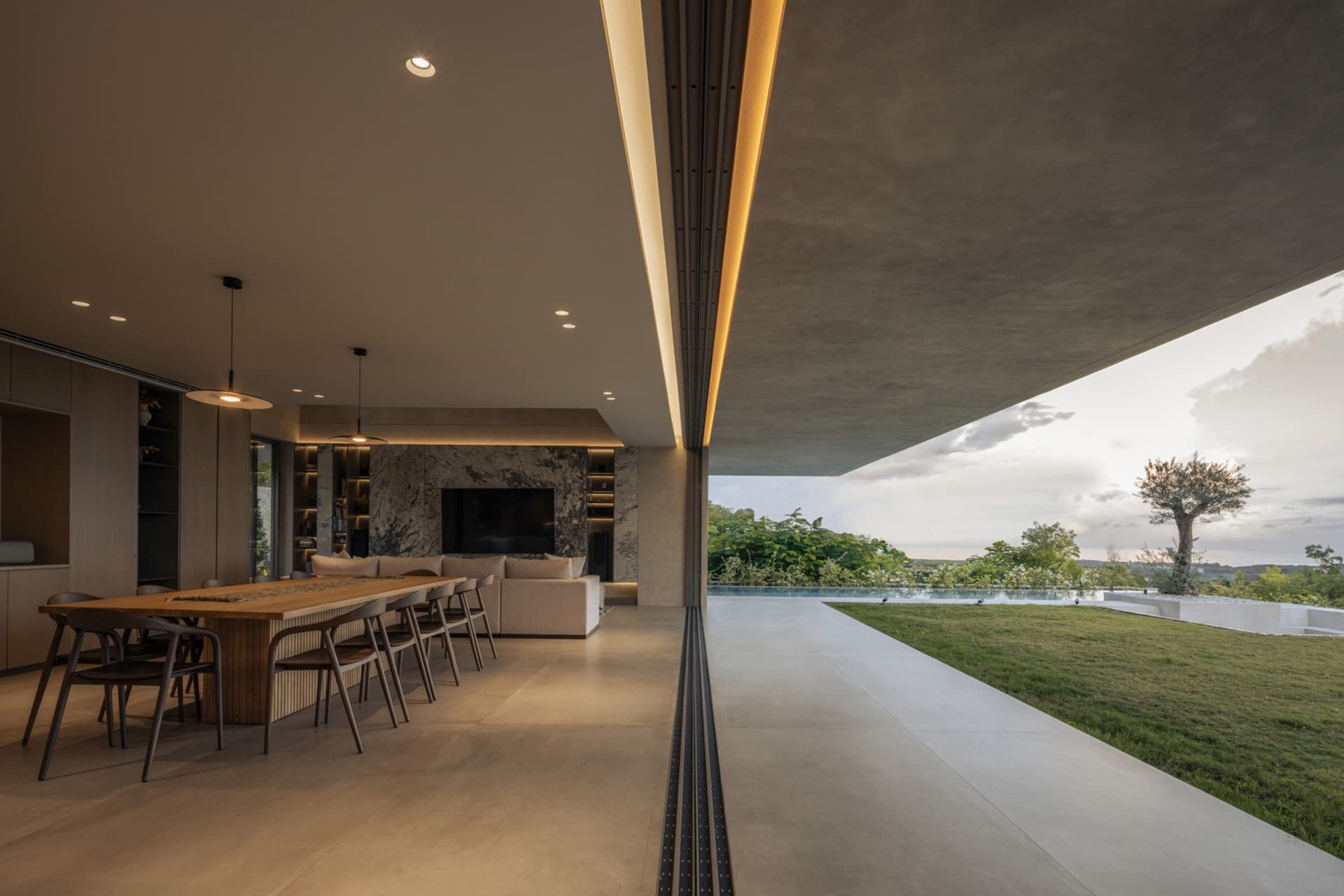 A modern living room with concrete and marble finishes, featuring a large terrace overlooking a lush outdoor area under a clo