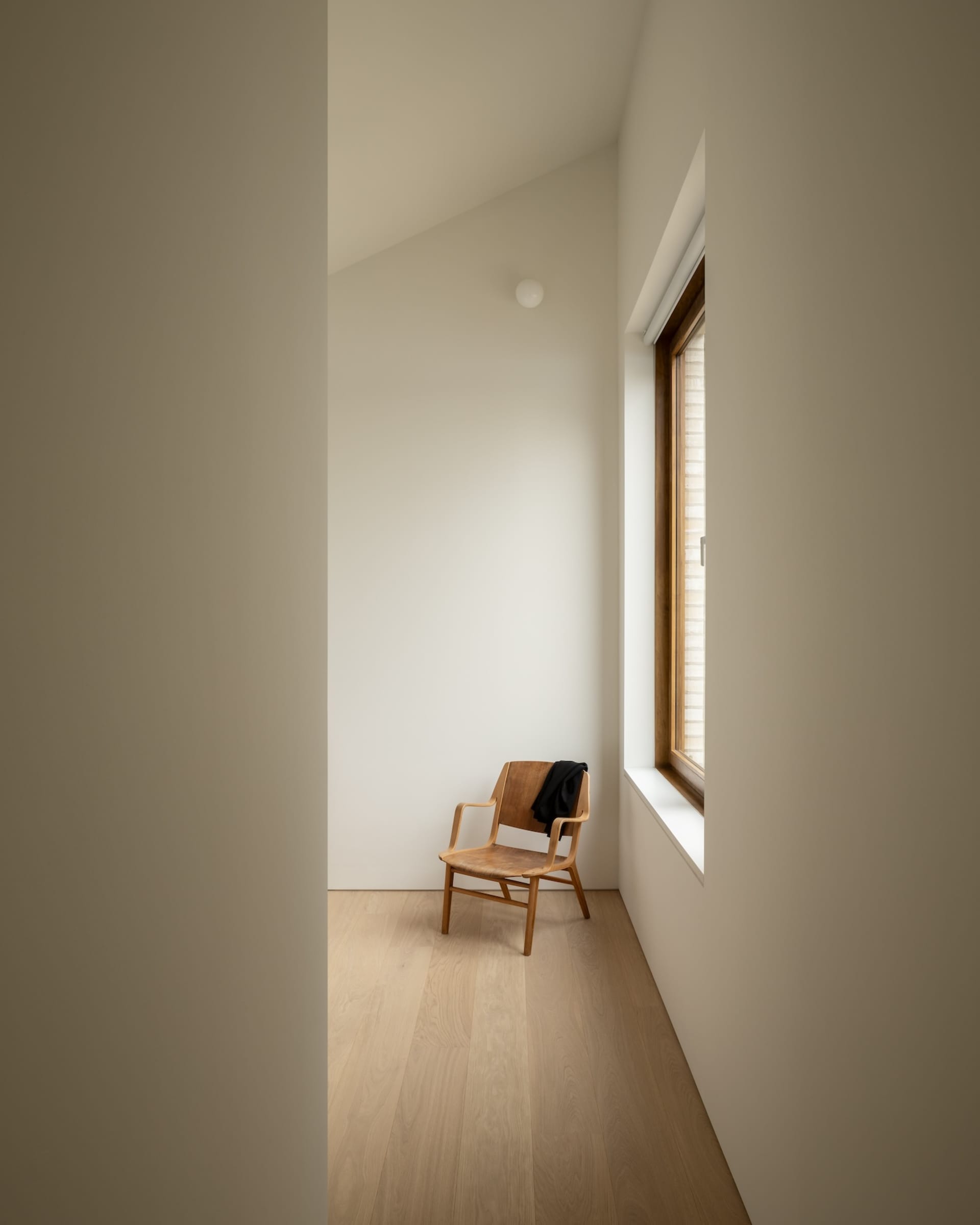 A minimalist bedroom with a wooden chair and a window.