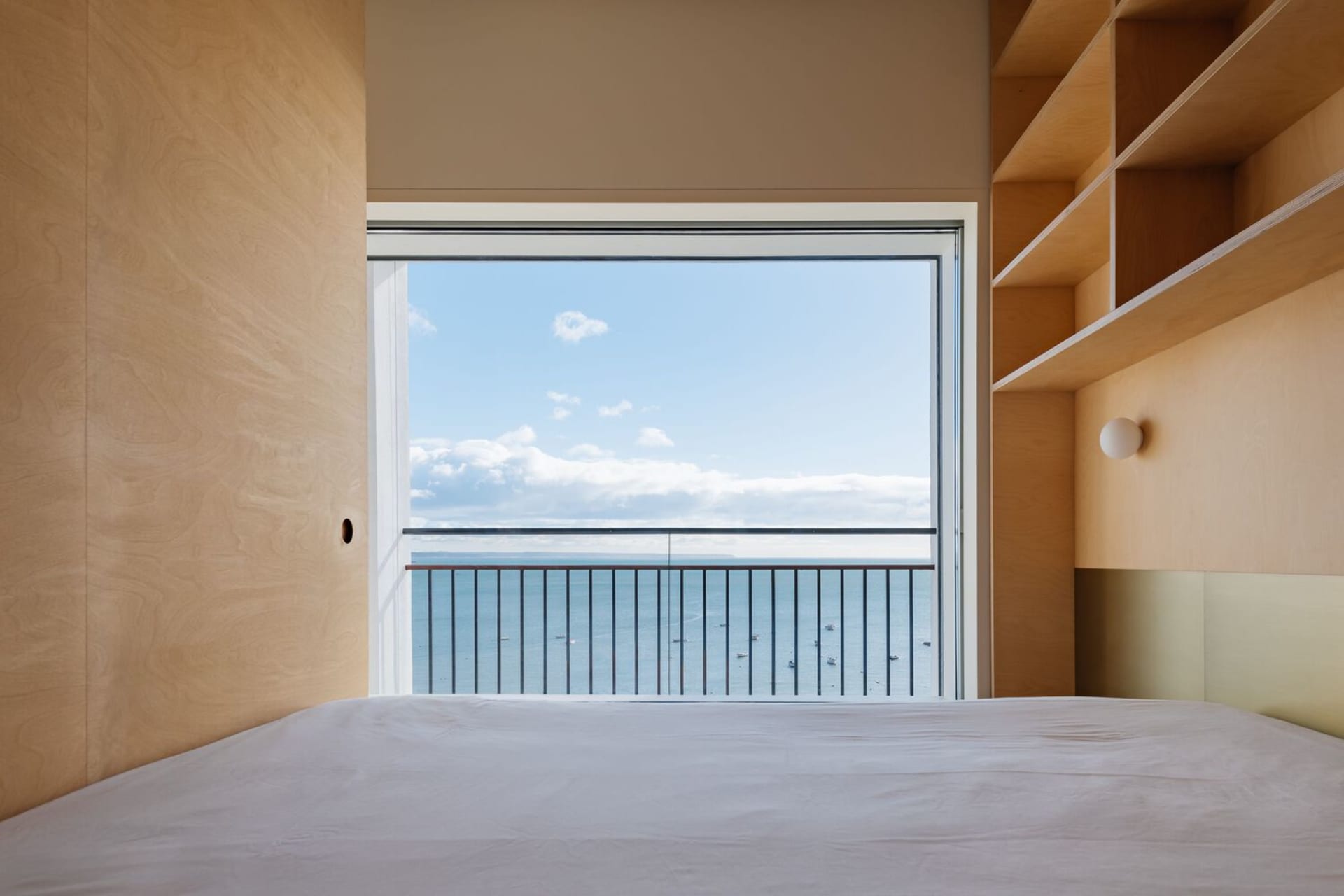 A minimalist bedroom featuring a large window with an ocean view, wood walls, and a bed.