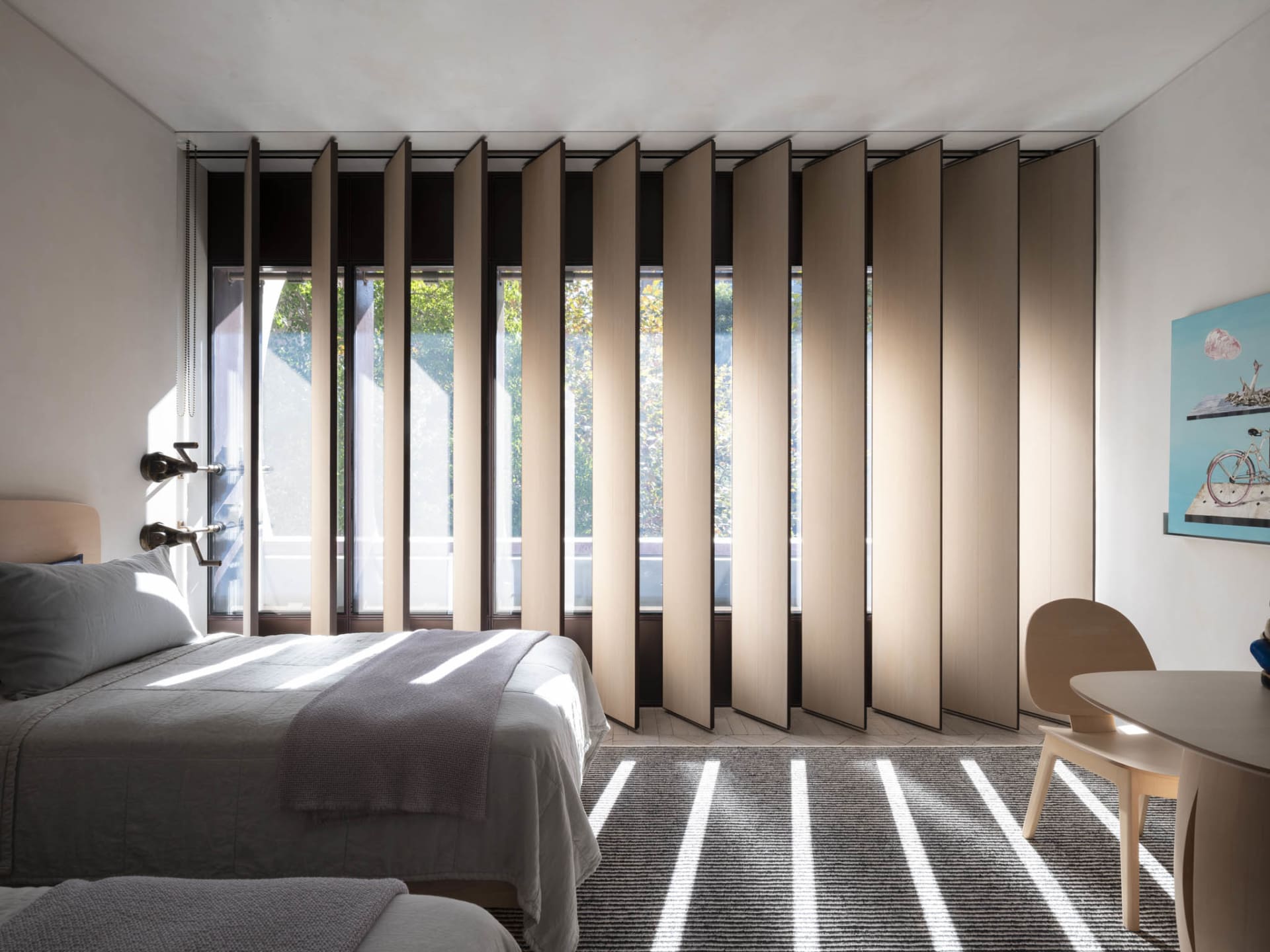 A modern bedroom featuring a bed with white sheets, a wooden headboard, and a large window with wooden blinds.