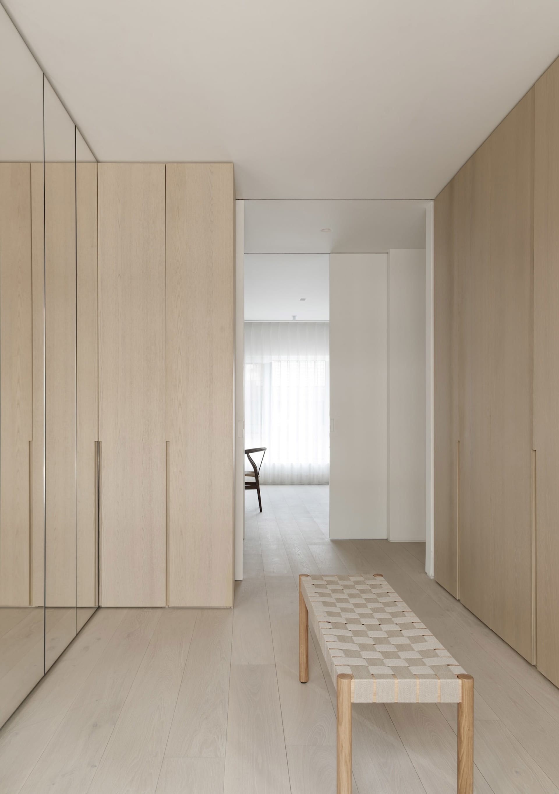 A modern closet interior with light-colored wooden cabinets and a woven seat bench in a minimalist design.