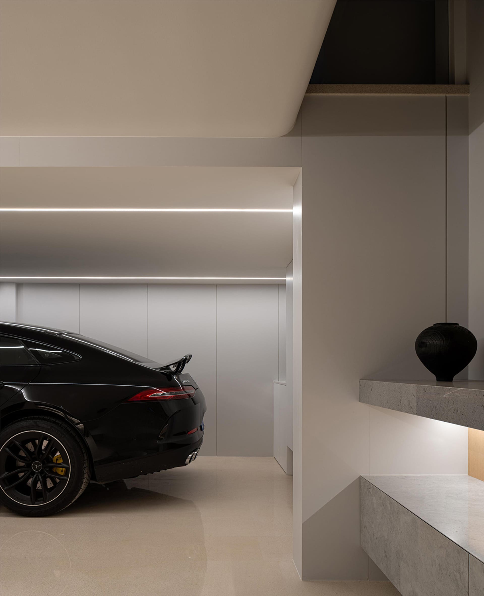 Modern garage interior with a sleek black car, concrete flooring, and minimalist design.