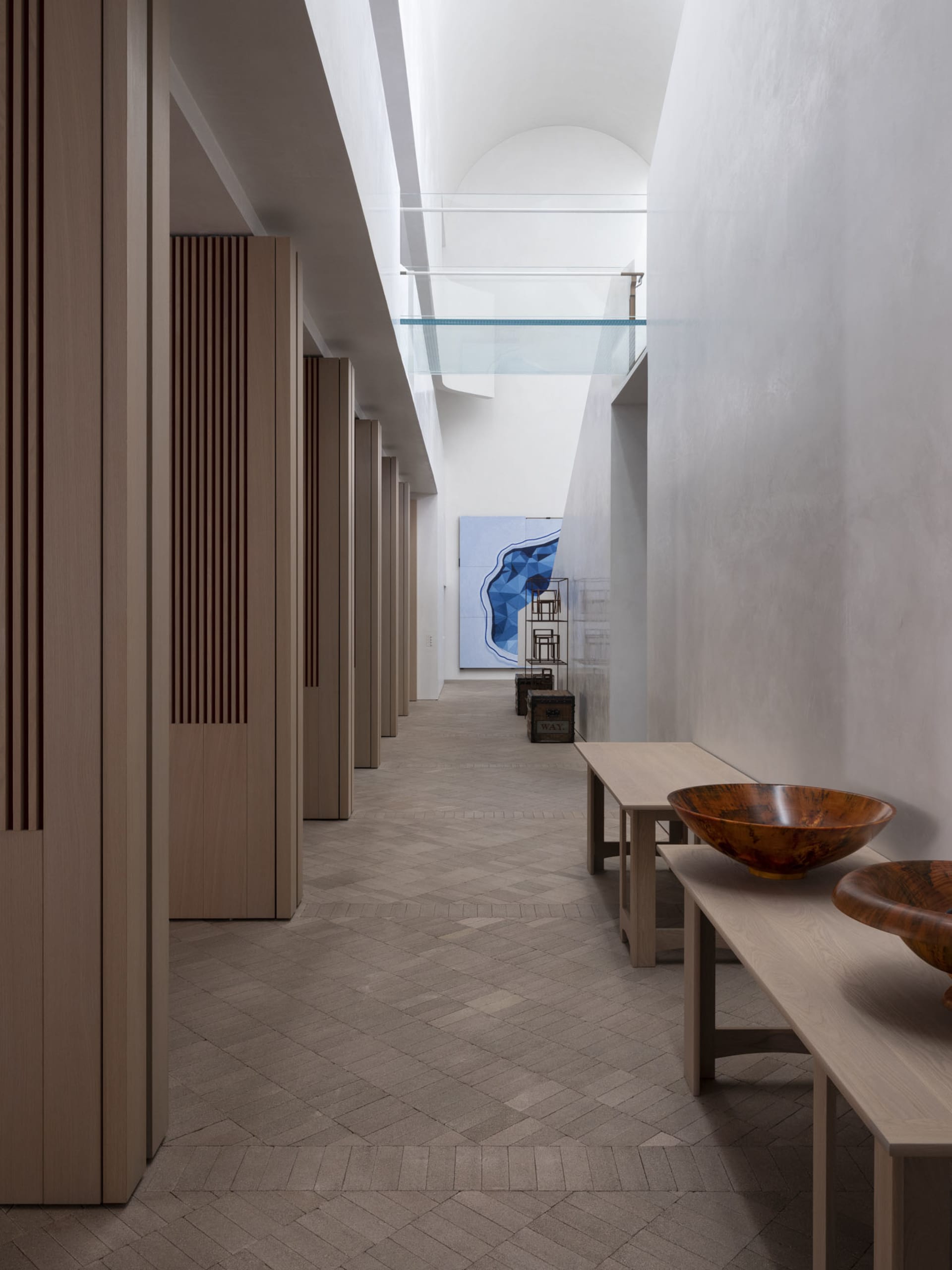 A modern interior design with concrete walls, wooden benches, and glass partitions in a long hallway-like space.