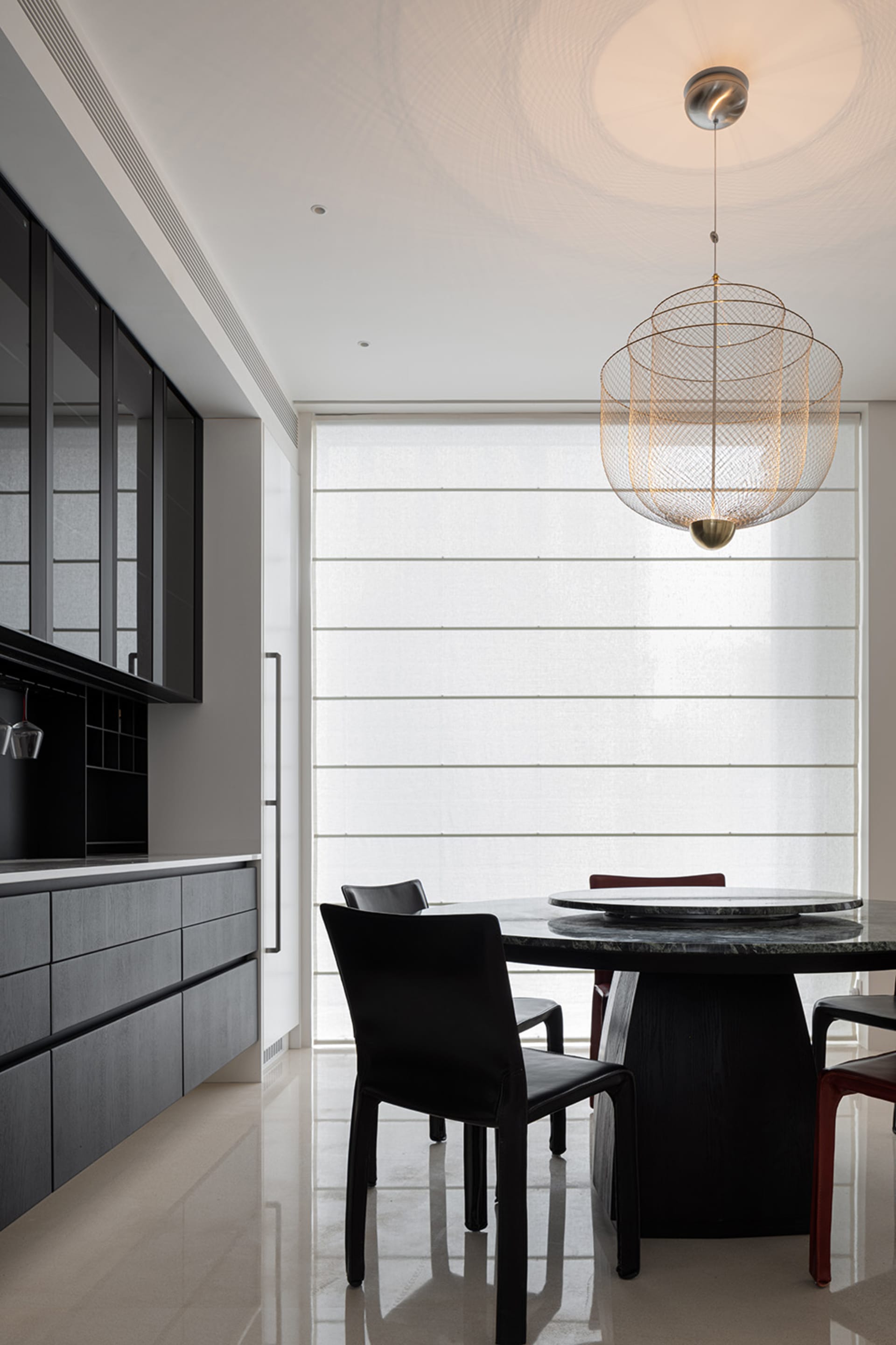 Modern kitchen interior featuring a round table with a marble top and black chairs, illuminated by a hanging lamp with a uniq