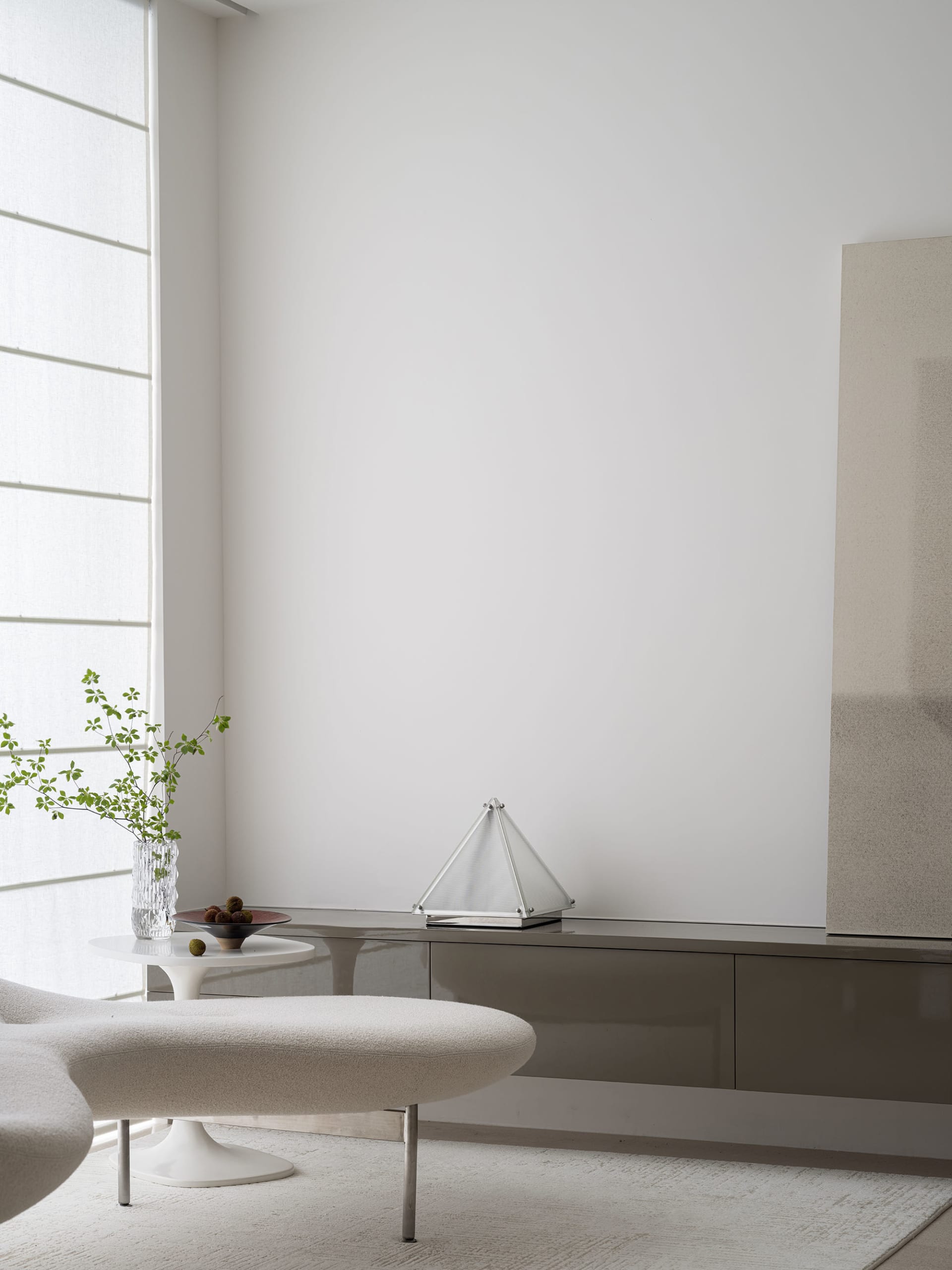 Modern minimalist living room featuring white furniture, a sleek glass cabinet, and a white ottoman with a white vase contain