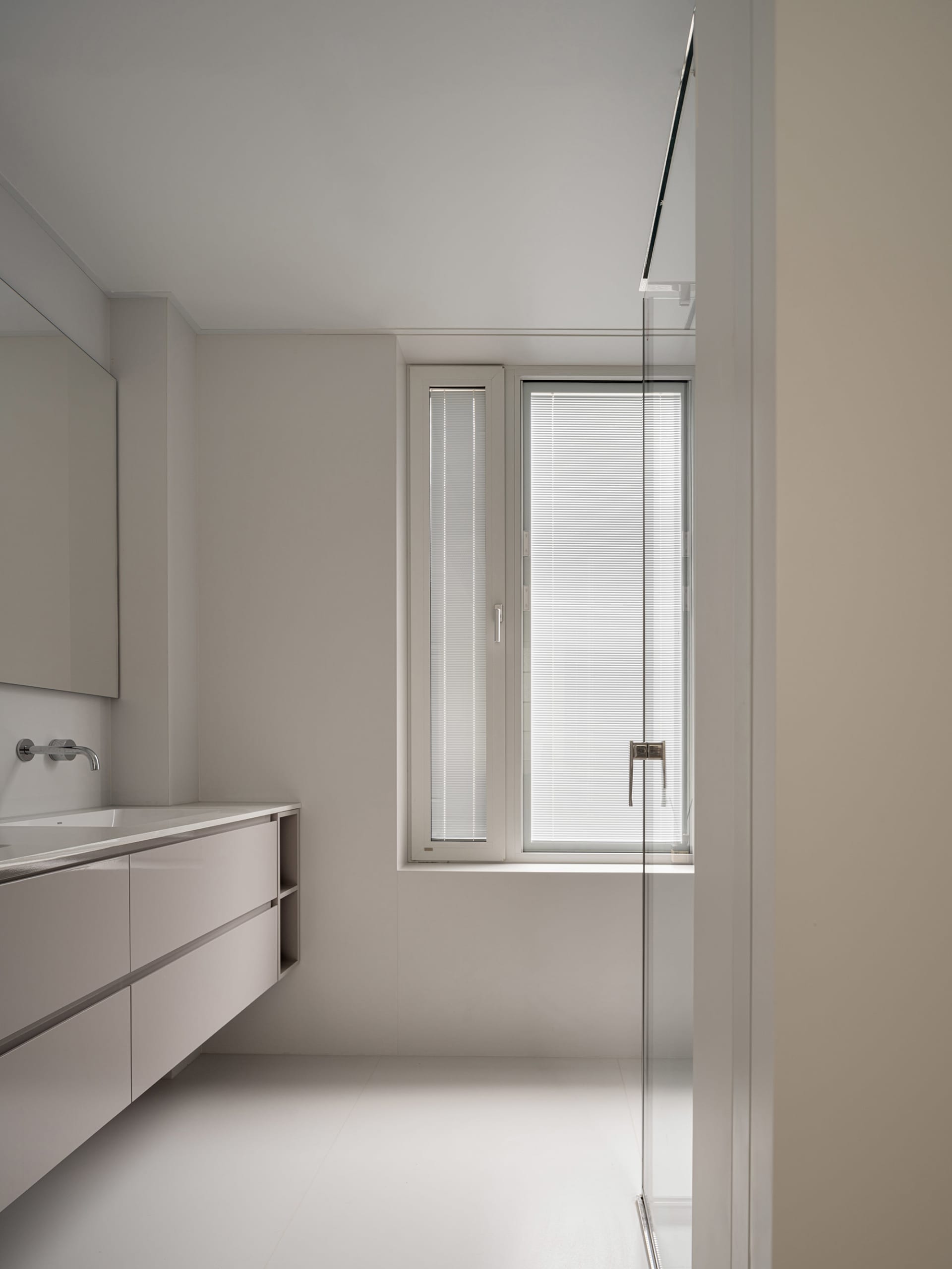 A minimalist white bathroom with a sleek design, featuring white walls, ceiling, floor, and a large rectangular window with b