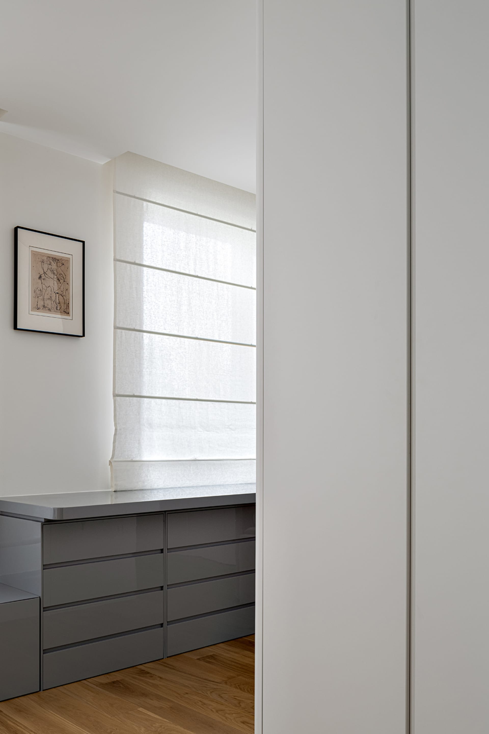 Modern gray kitchen cabinets situated by a window sill with sheer white curtains.