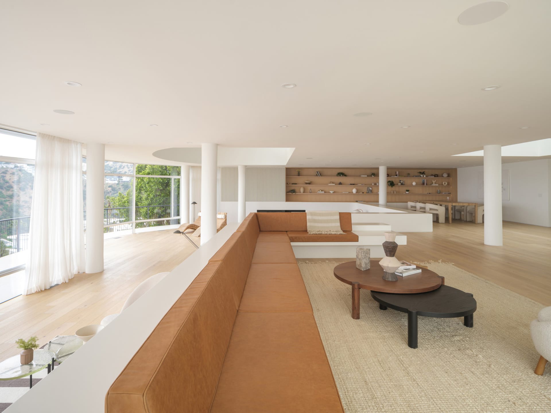 Modern living room featuring a long brown leather sofa, wooden flooring, and white walls.