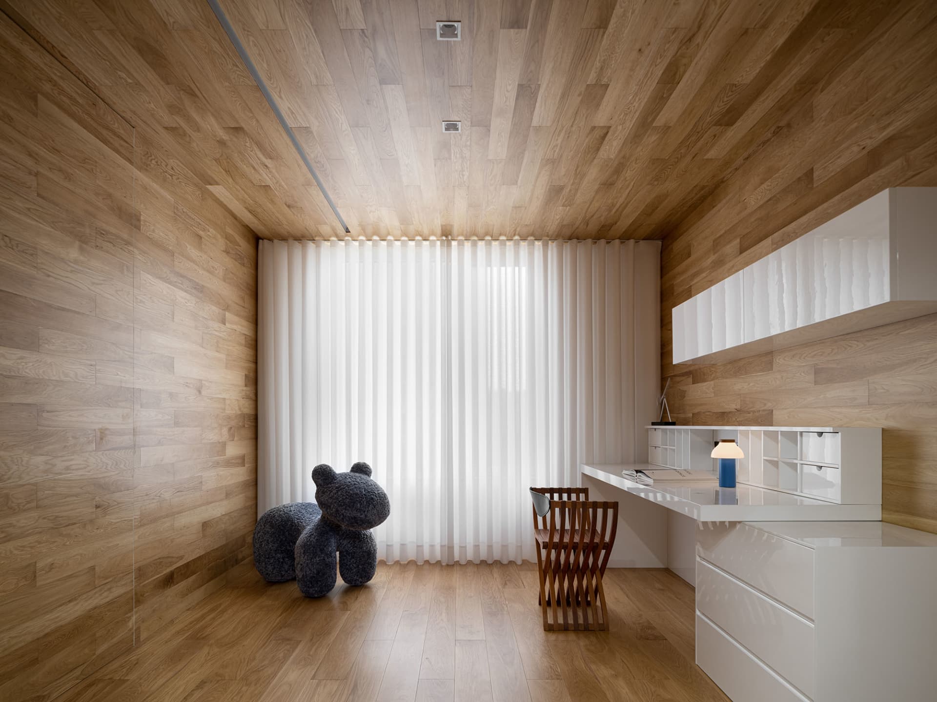 現代簡約居家辦公室,木質地板與牆面,搭配白色書桌與椅子,以及一隻毛絨玩具馬。
