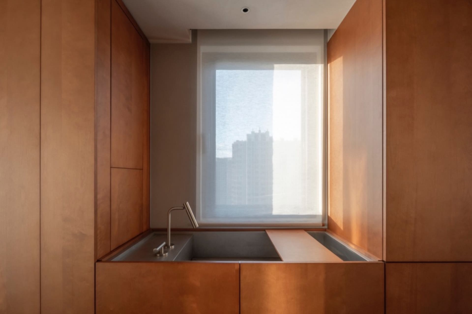 Modern residential kitchen with wooden cabinets, a stainless steel sink, and a window with sheer curtains.