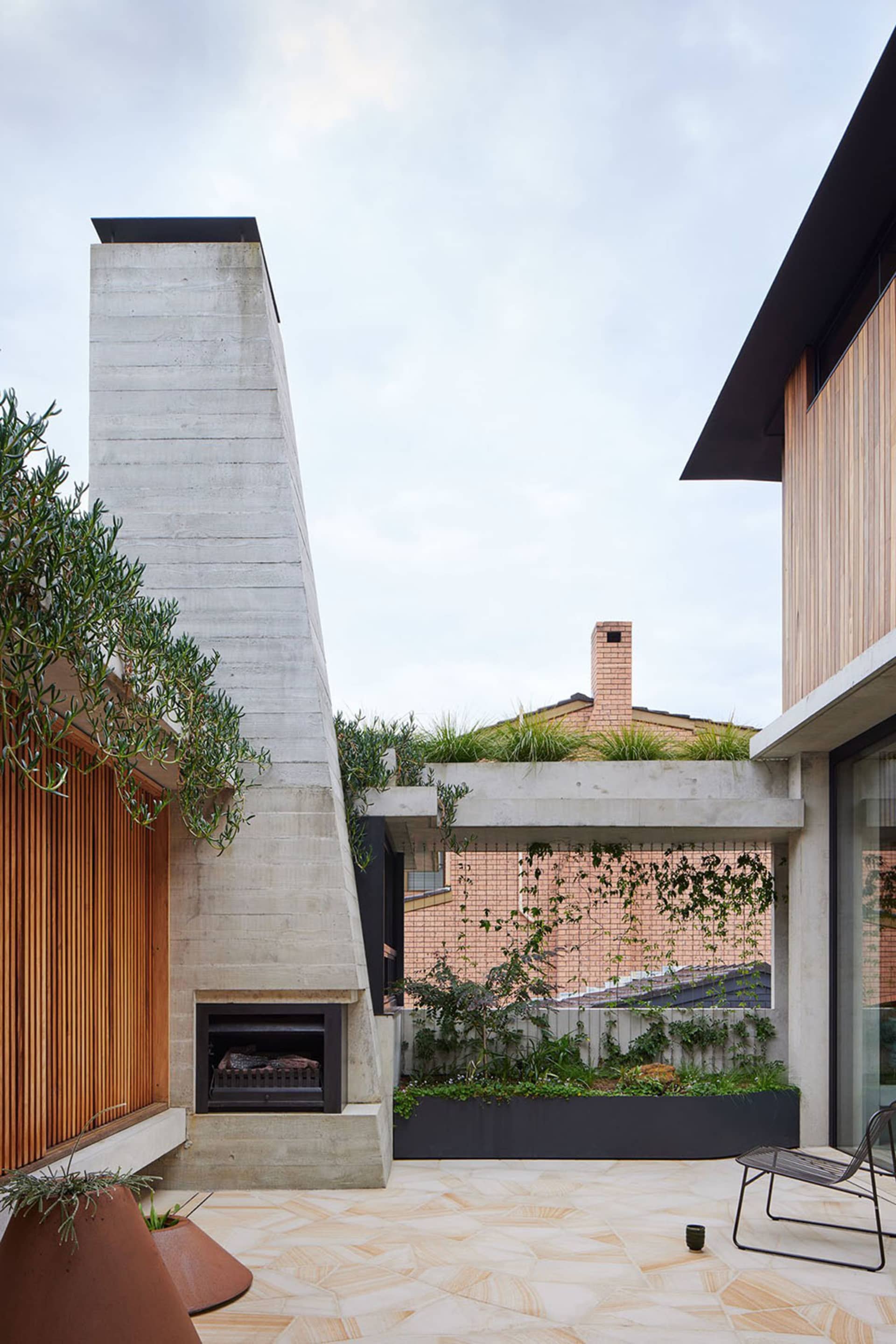 Modern exterior space featuring a concrete fireplace, roof garden with greenery, and wooden accents.