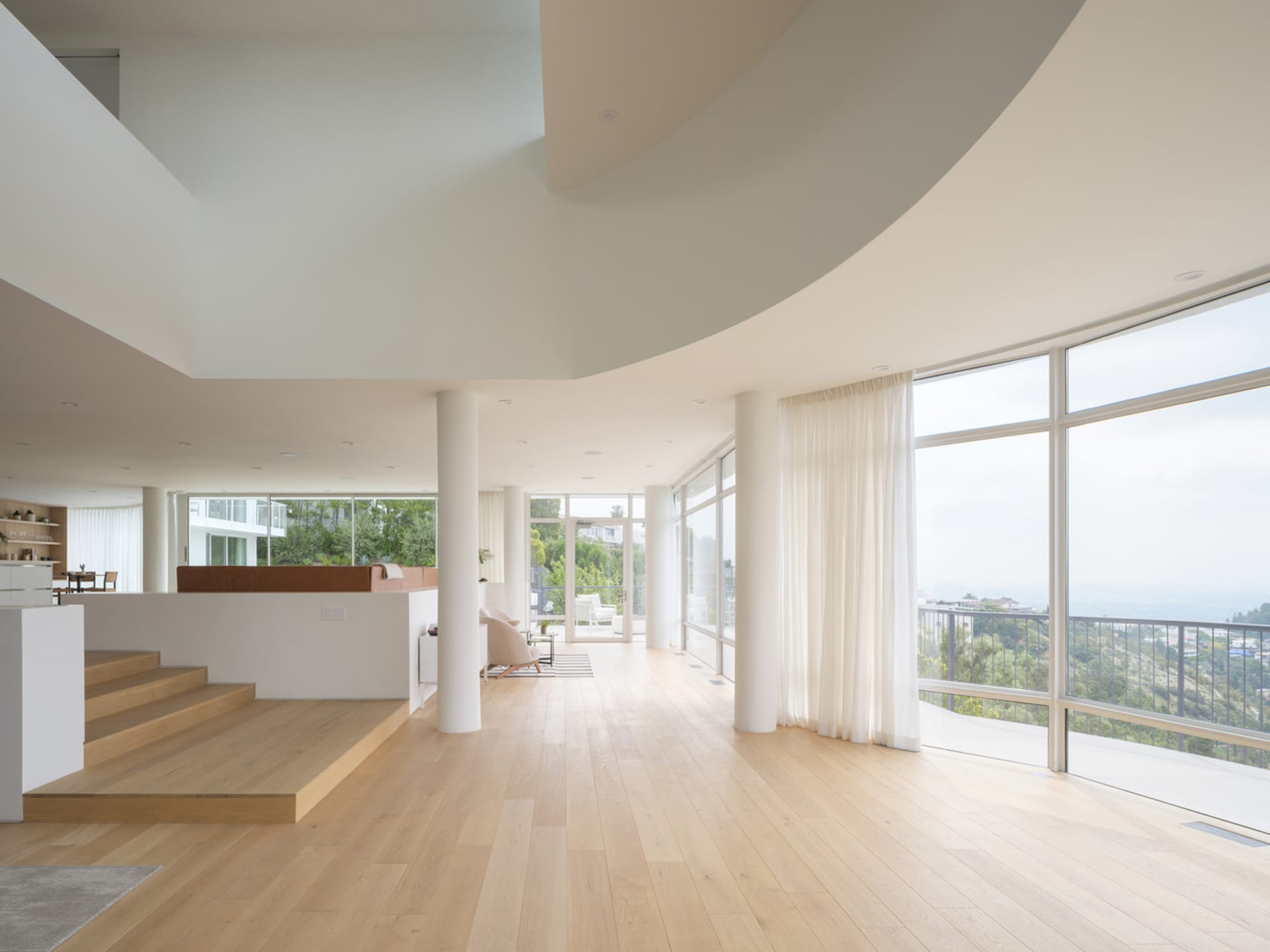 A modern living room with a wooden floor and white curtains.