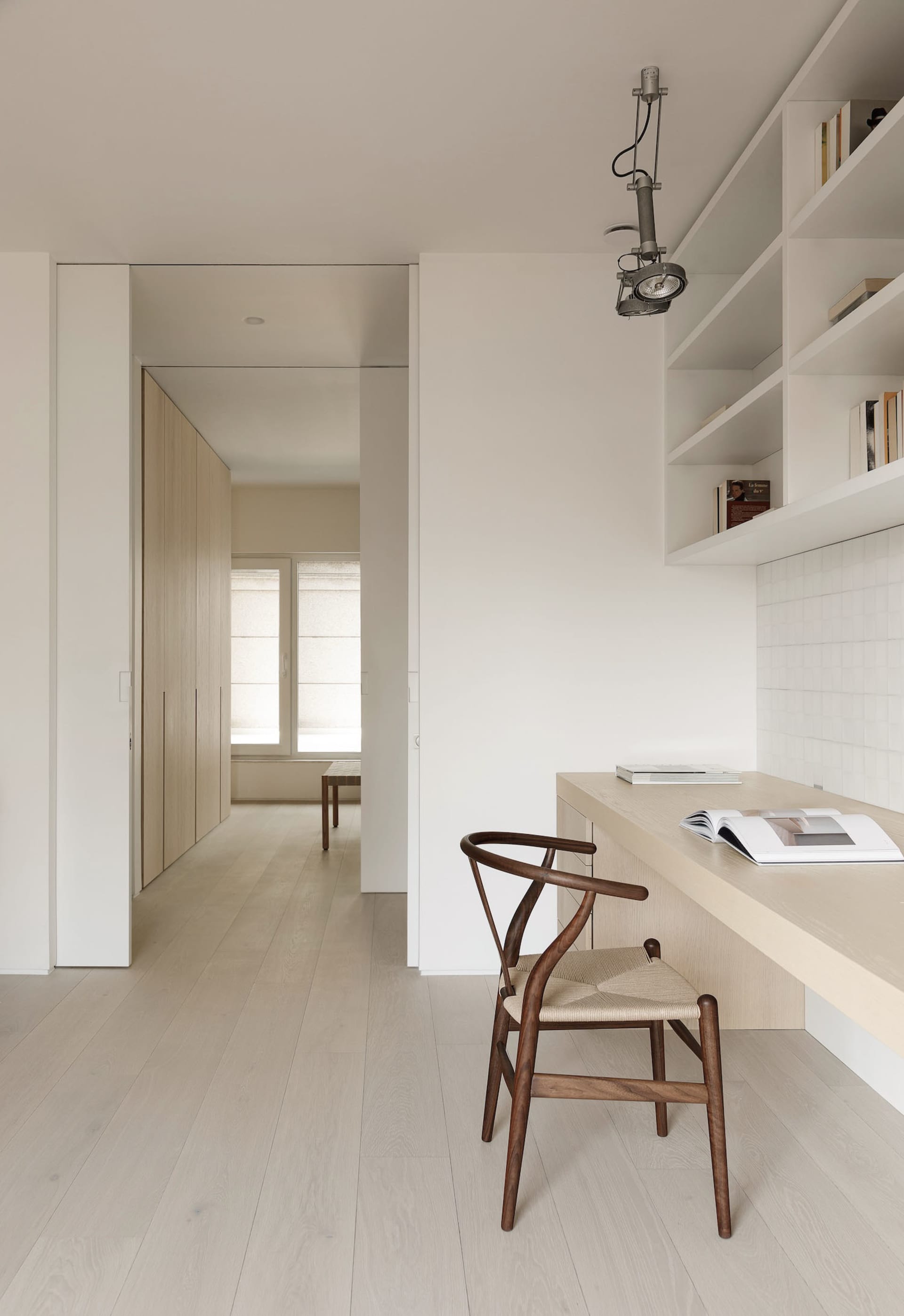 Modern minimalist home office featuring a wooden desk, metal chair, and open shelving.