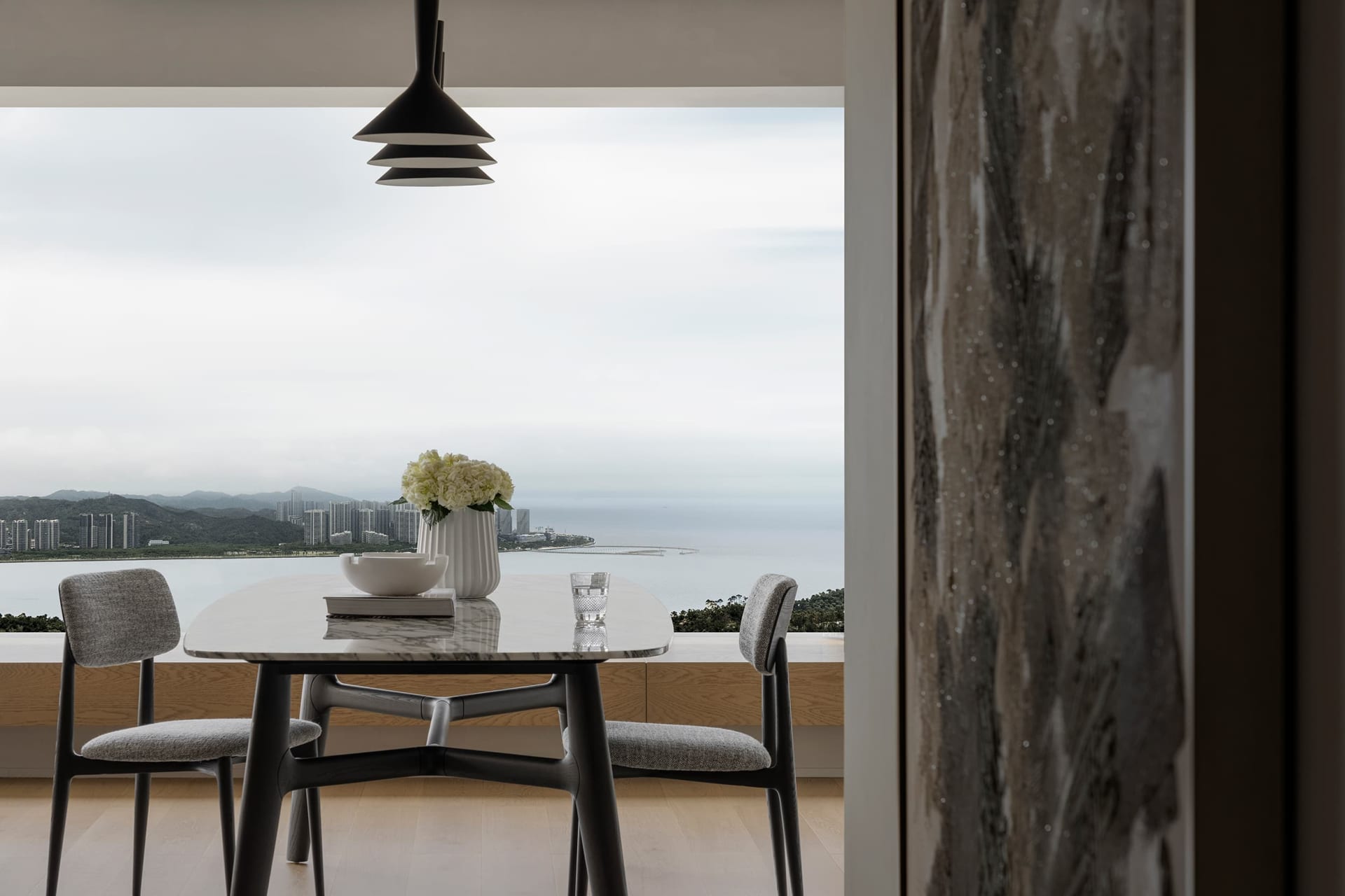 A modern dining table with a marble top and fabric upholstered chairs, set against a backdrop of a cityscape and ocean view.