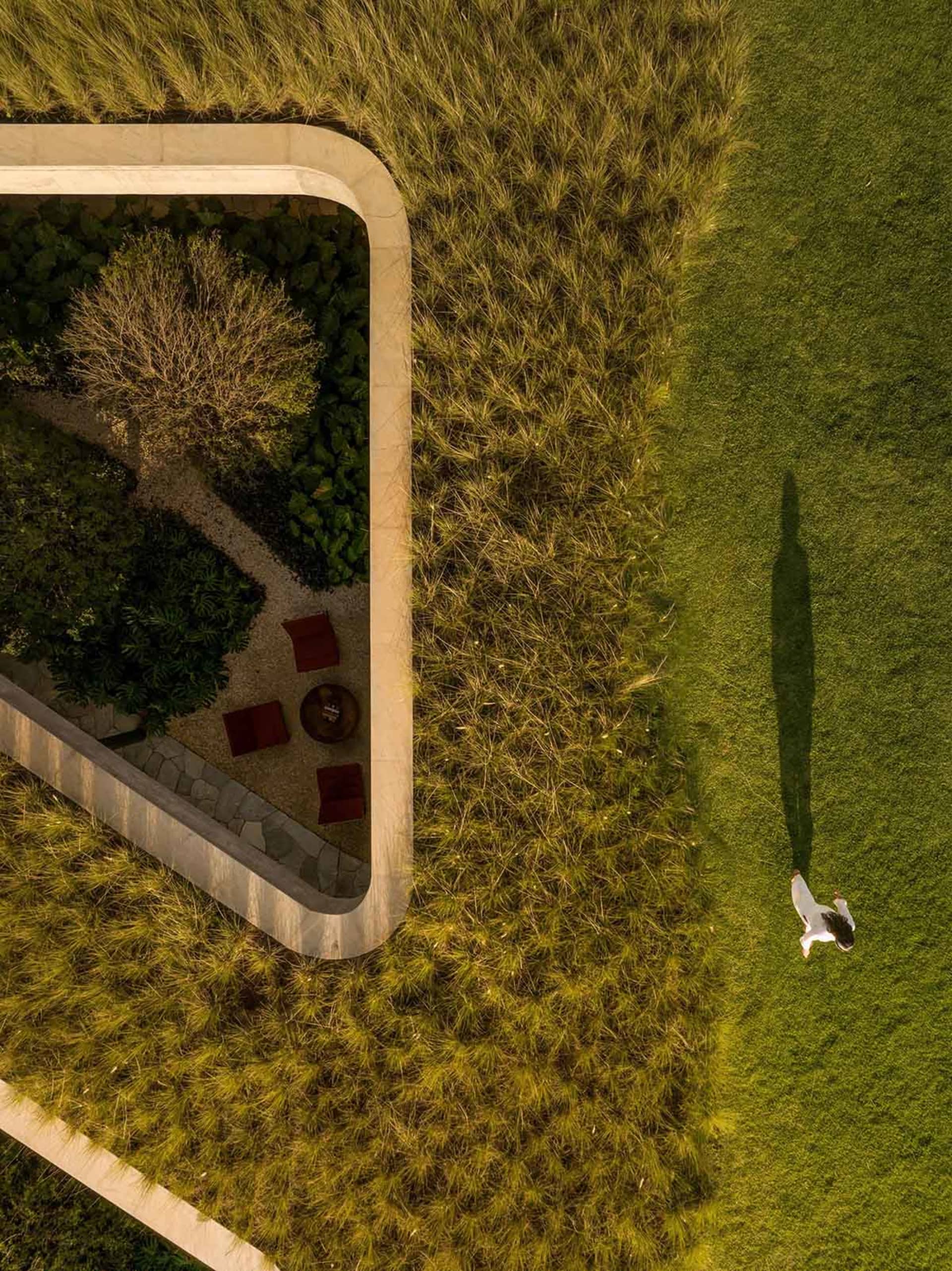Aerial view of a modern landscape design featuring a green grass lawn bordered by concrete pathways and a small garden area w