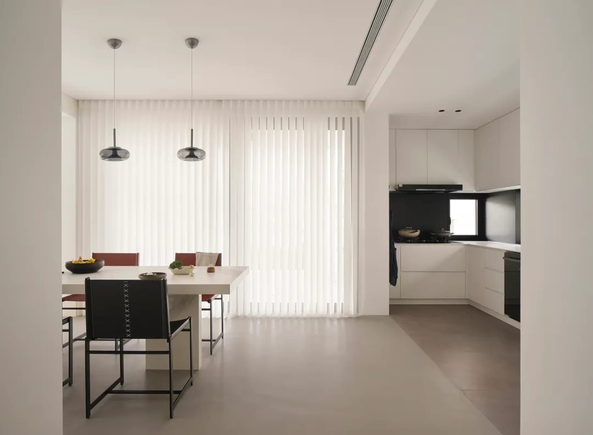 A modern, minimalist kitchen with a sleek white countertop and black pendant lights hanging above a dining table.