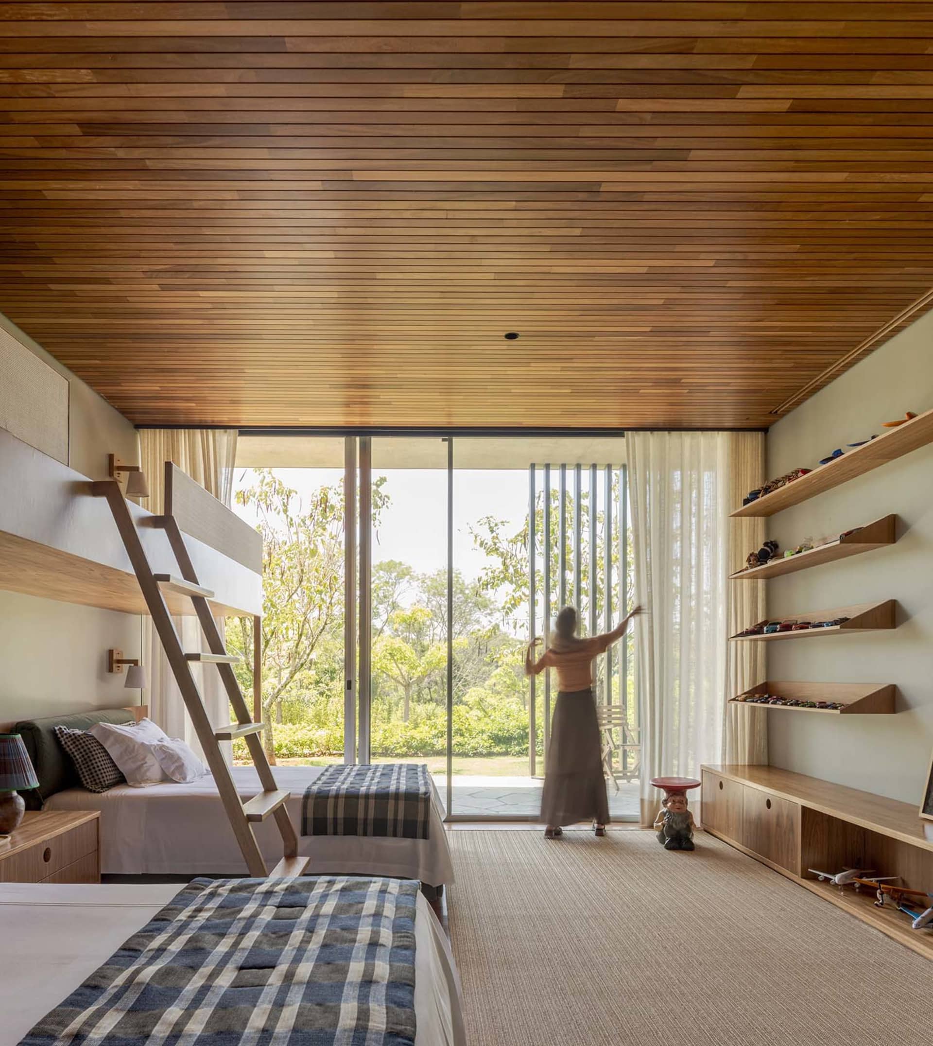 A modern bedroom with wooden furniture and a large window overlooking a green landscape.