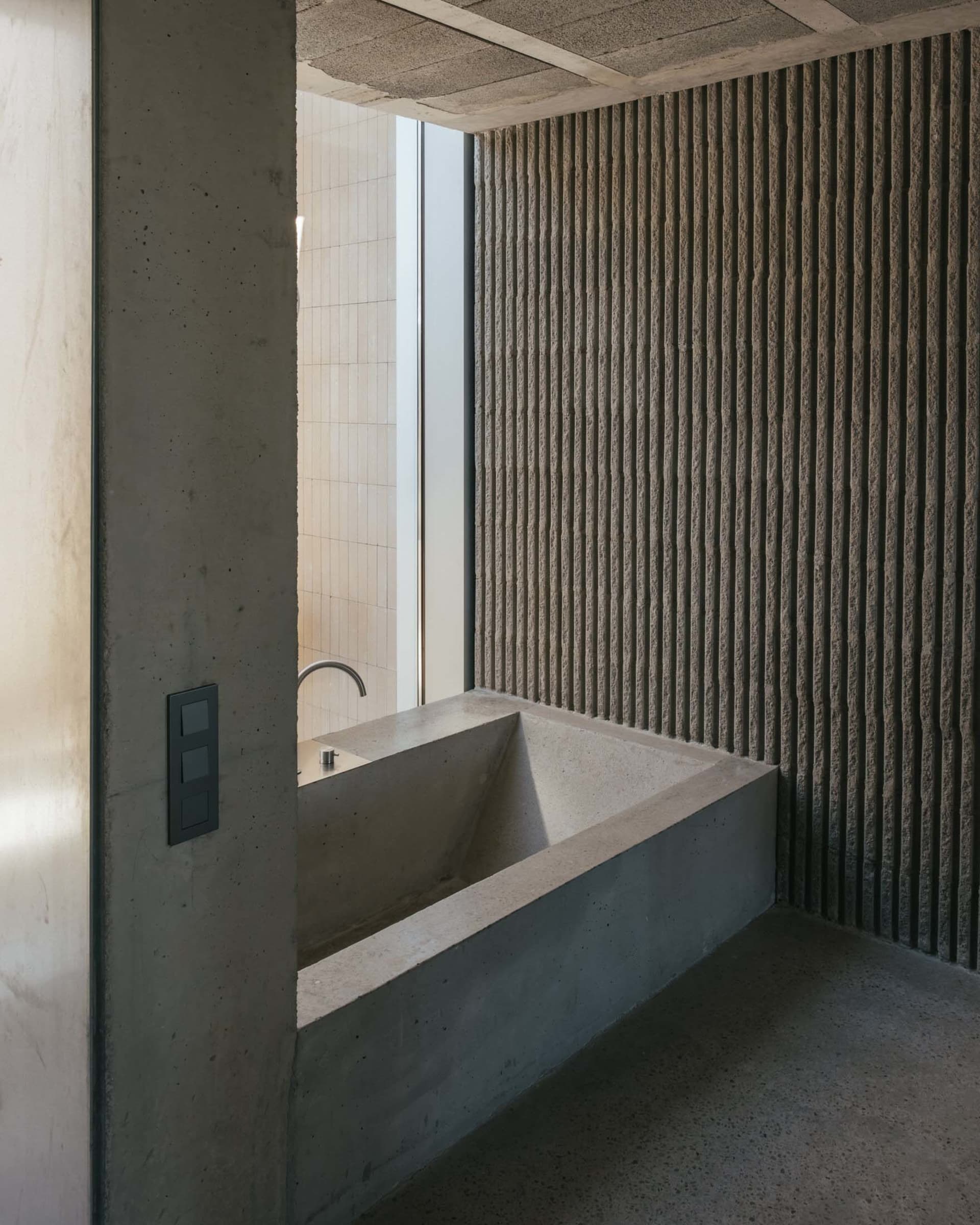 A modern, industrial-style bathroom featuring a concrete bathtub and textured wall.