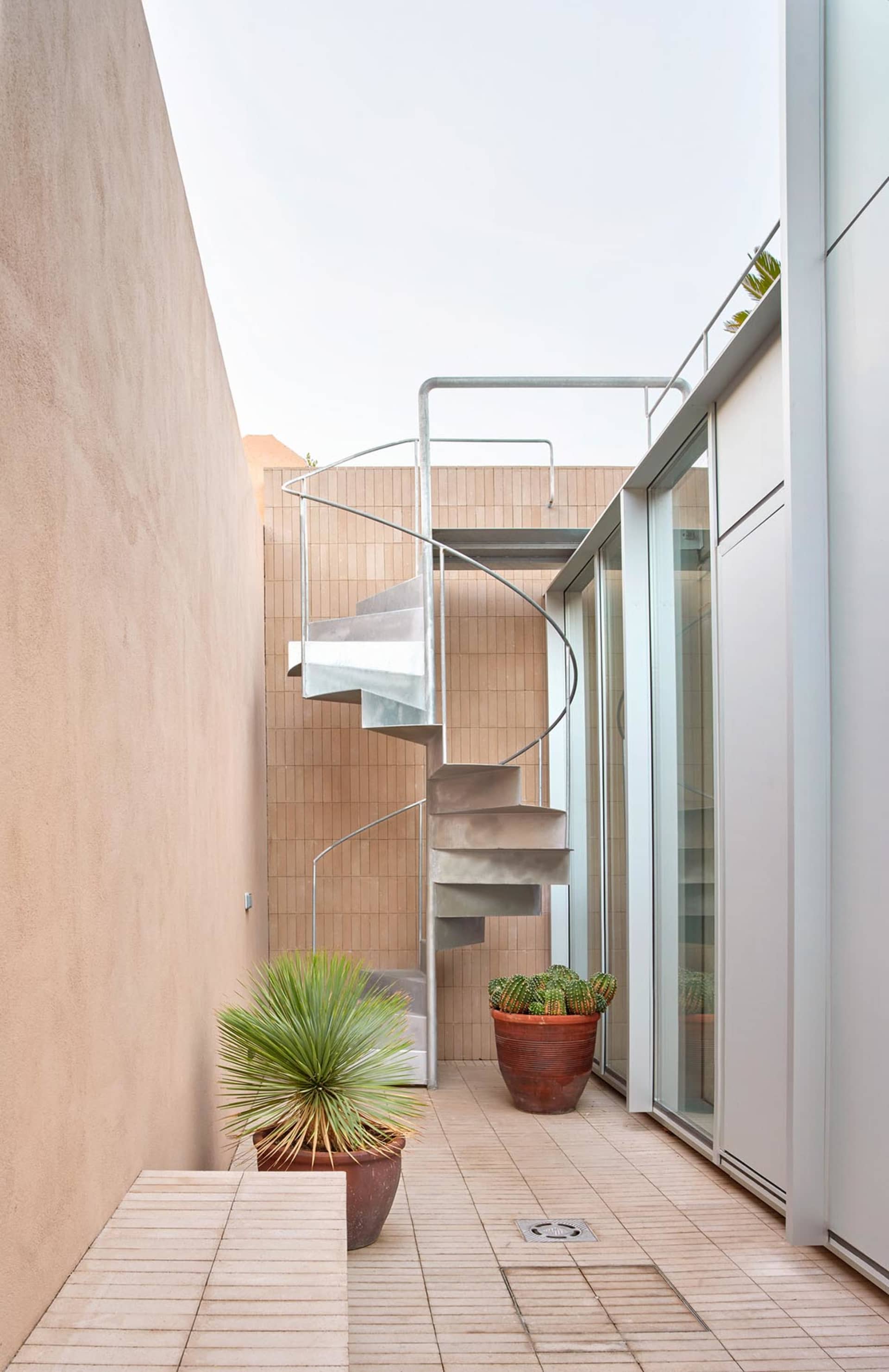 Modern metallic spiral staircase outside a building with a glass wall.