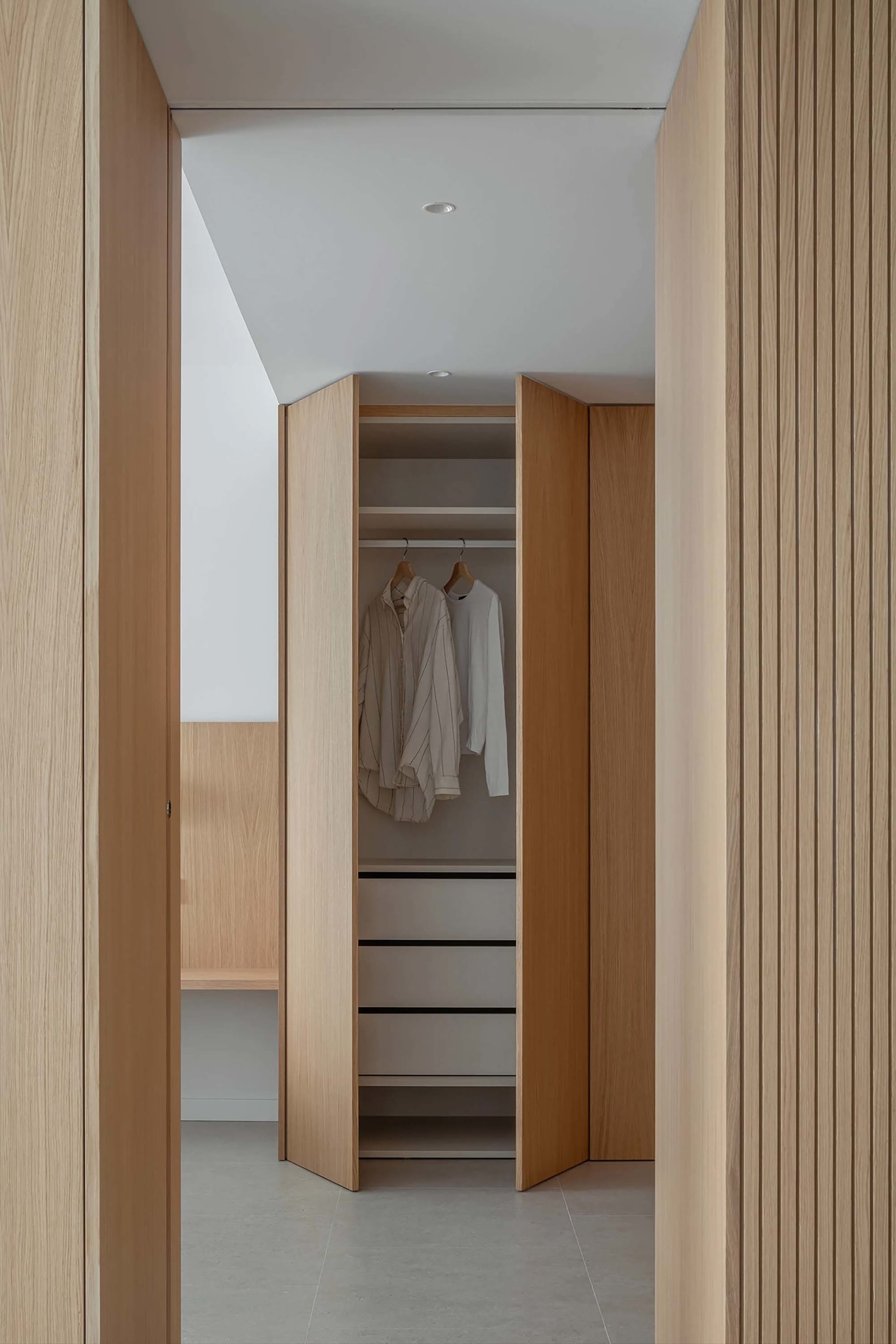 Modern-style walk-in closet with wooden hanging rails and minimalist design, featuring a white ceiling and grey floor tiles.