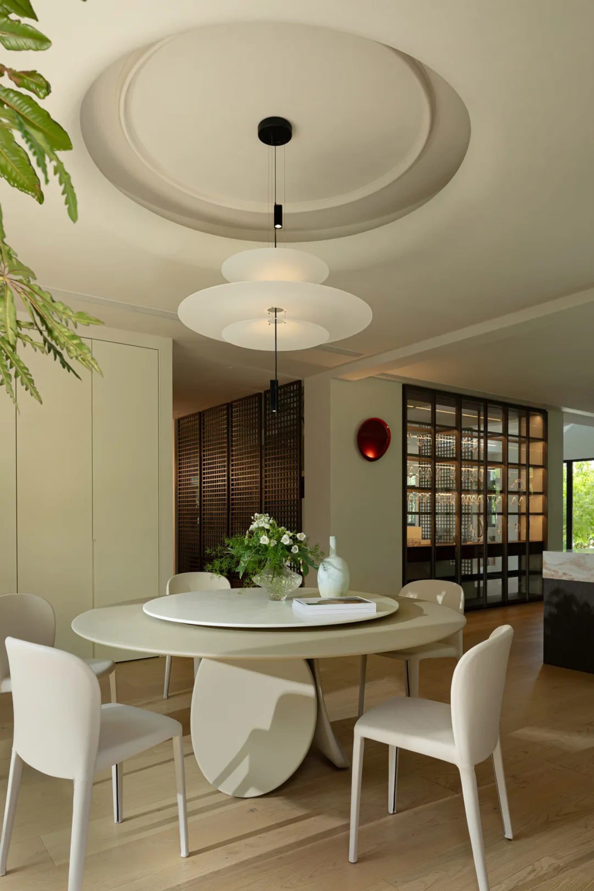 A modern, minimalist dining room with a round table, chairs, vases, and a decorative red wall light, featuring sleek, clean l