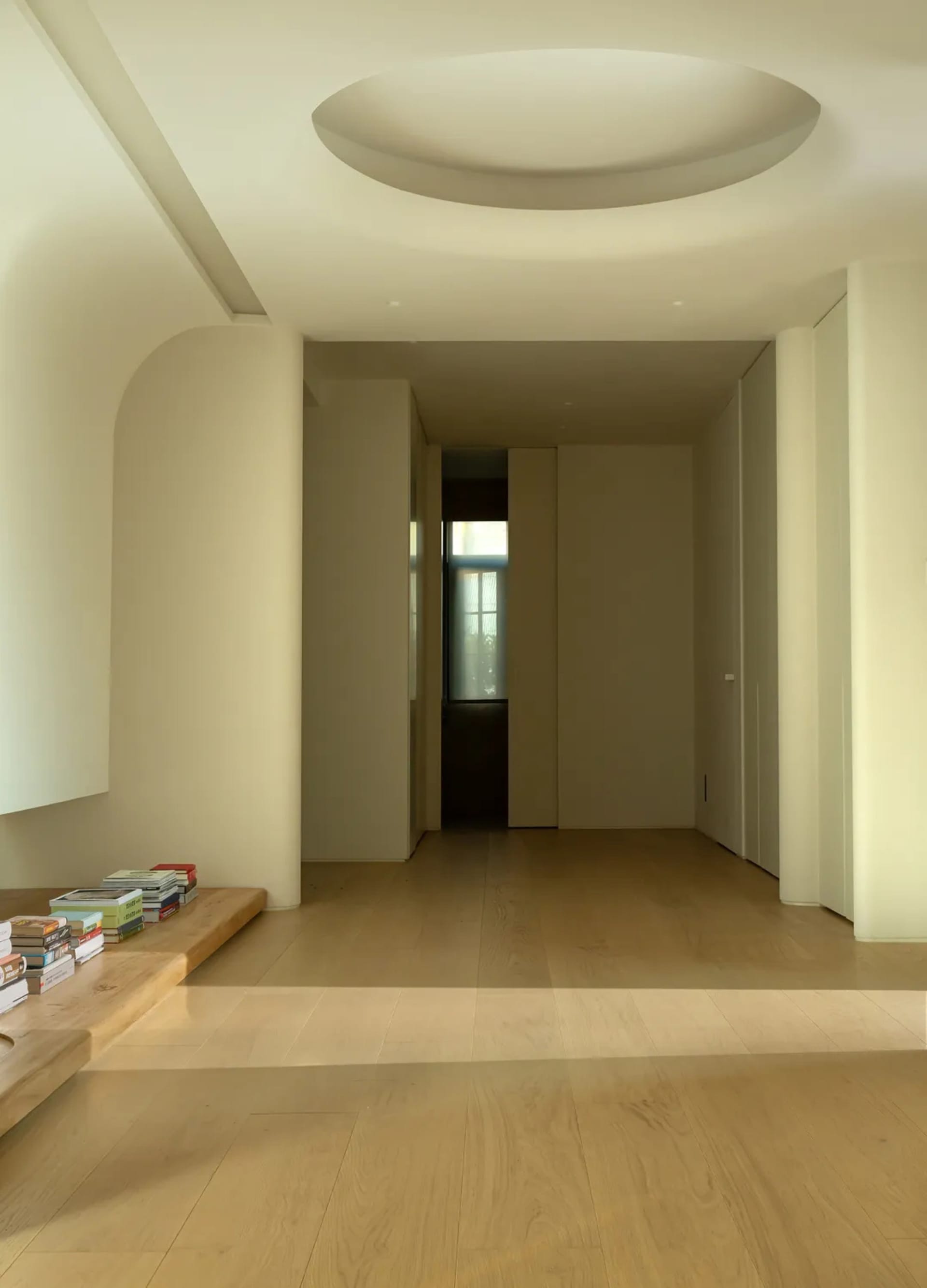 A minimalist interior with a wooden floor, arches, and a circular skylight.