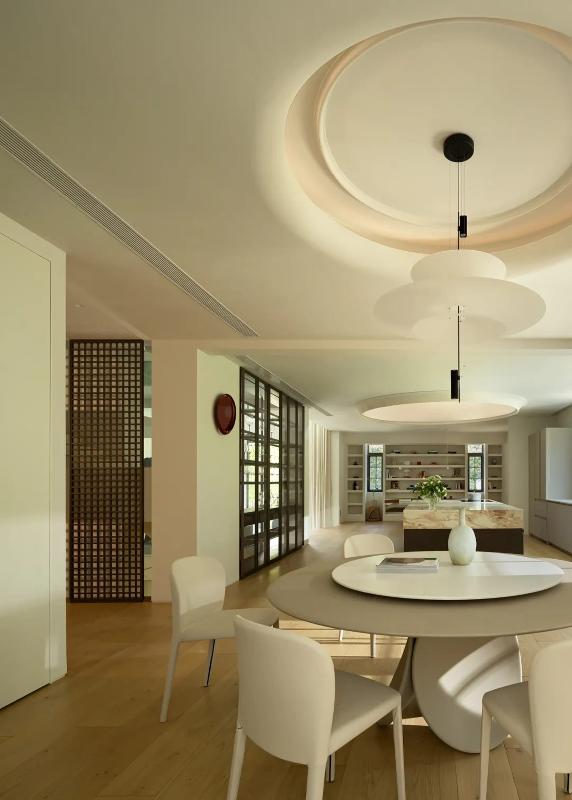A modern dining room featuring metal and plastic materials with a round table and chairs, a central pendant light, and a book