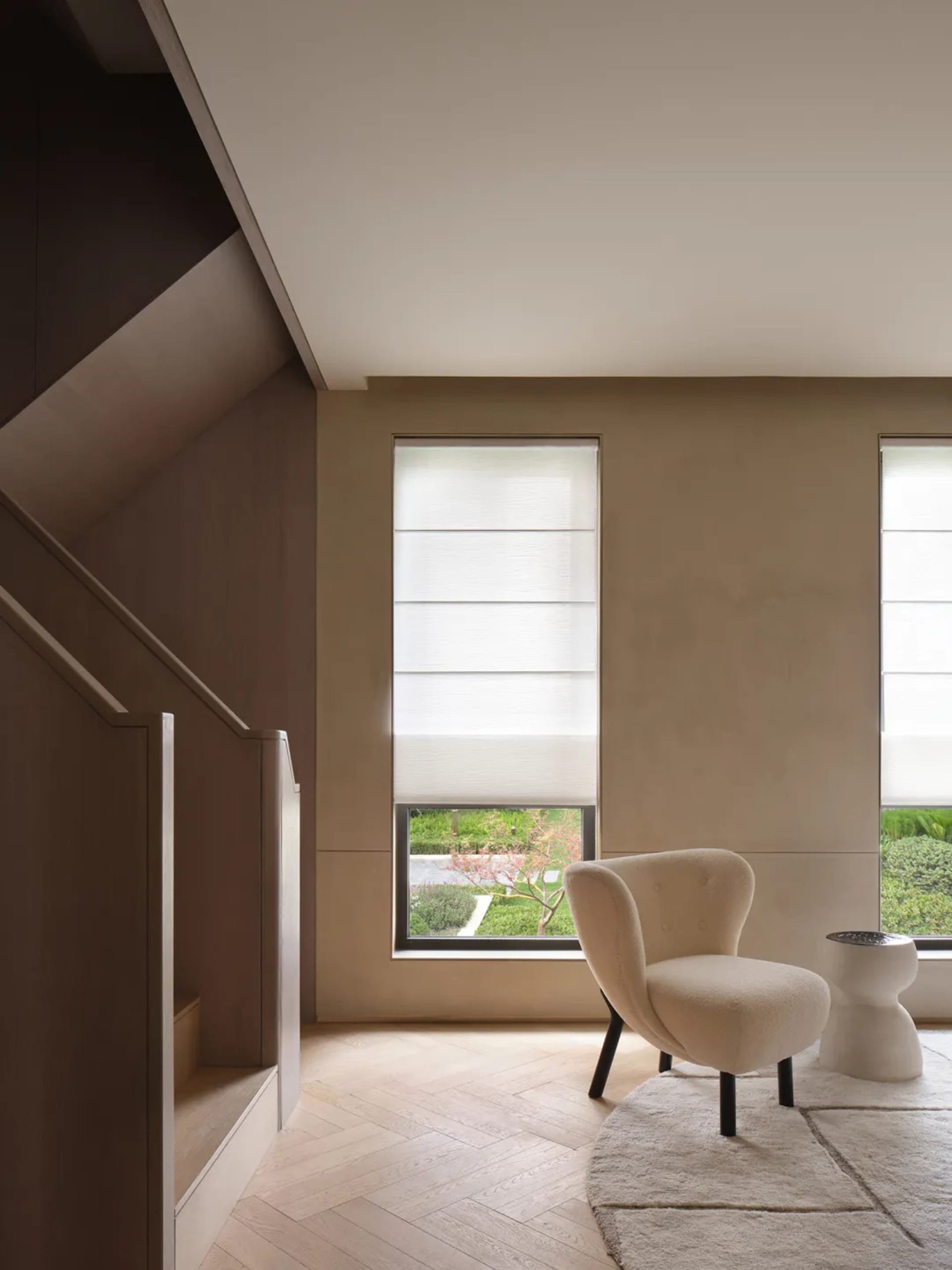 A modern living room featuring a tan stone floor, beige carpet, textured white walls, white curtains, and a white chair with