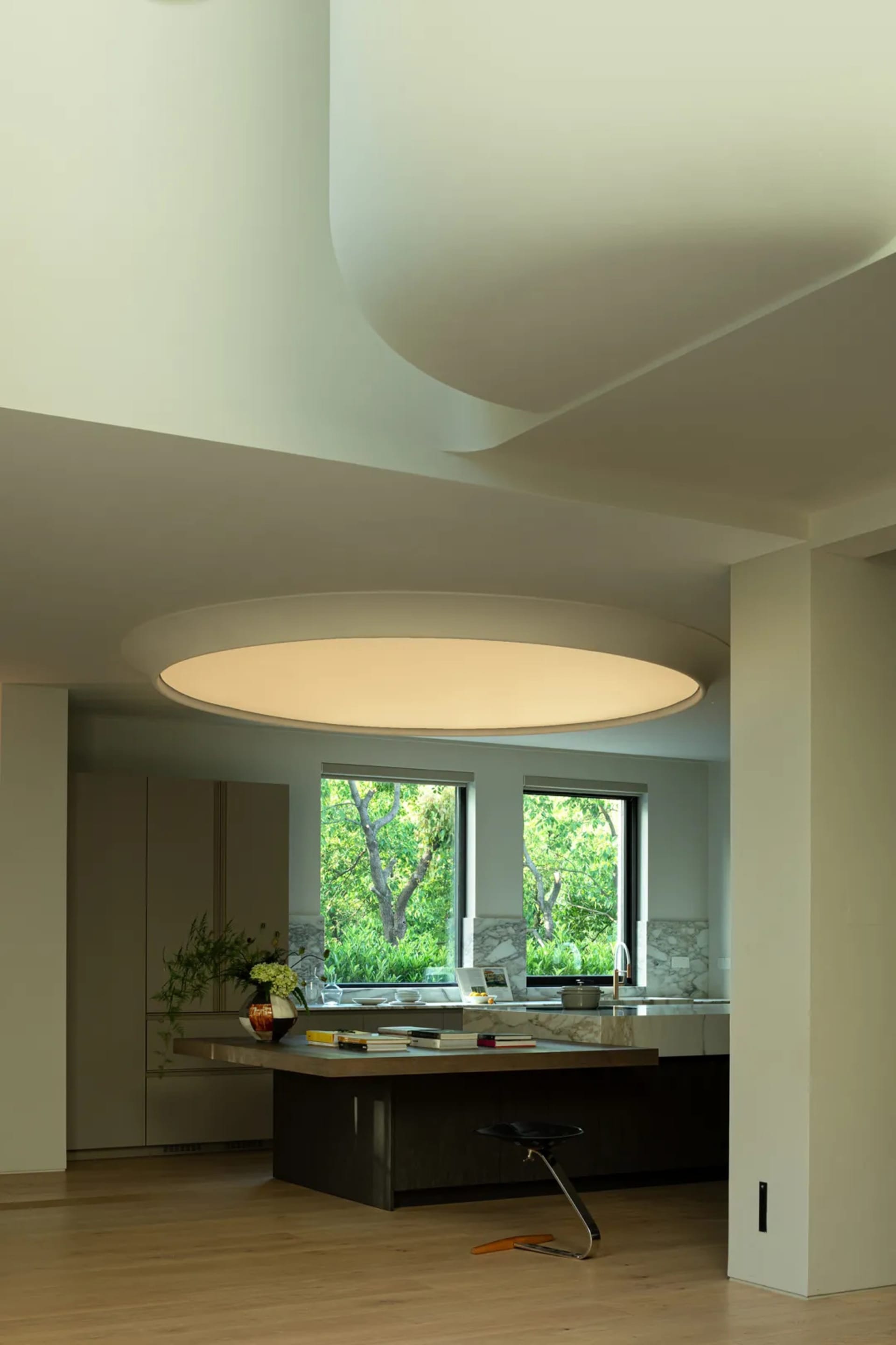 A modern residential kitchen featuring a marble countertop and floor-to-ceiling windows with a view of greenery outside.