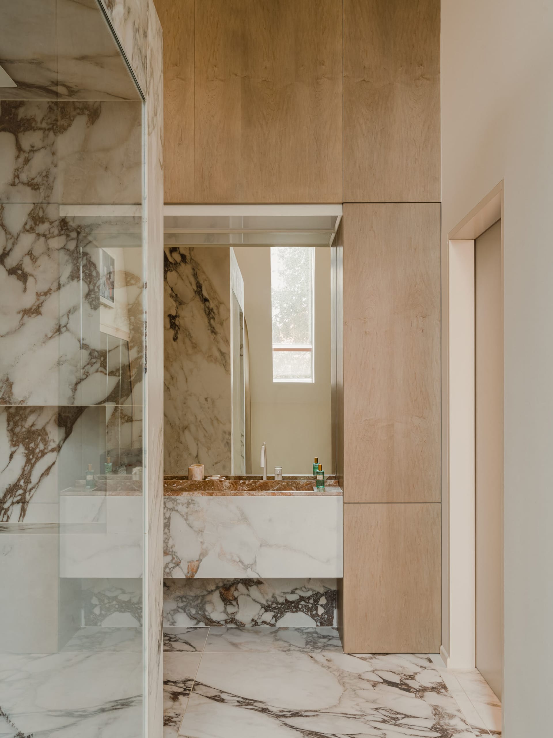 A sleek, contemporary bathroom with marble tiles, a glass shower enclosure, and wooden cabinetry.
