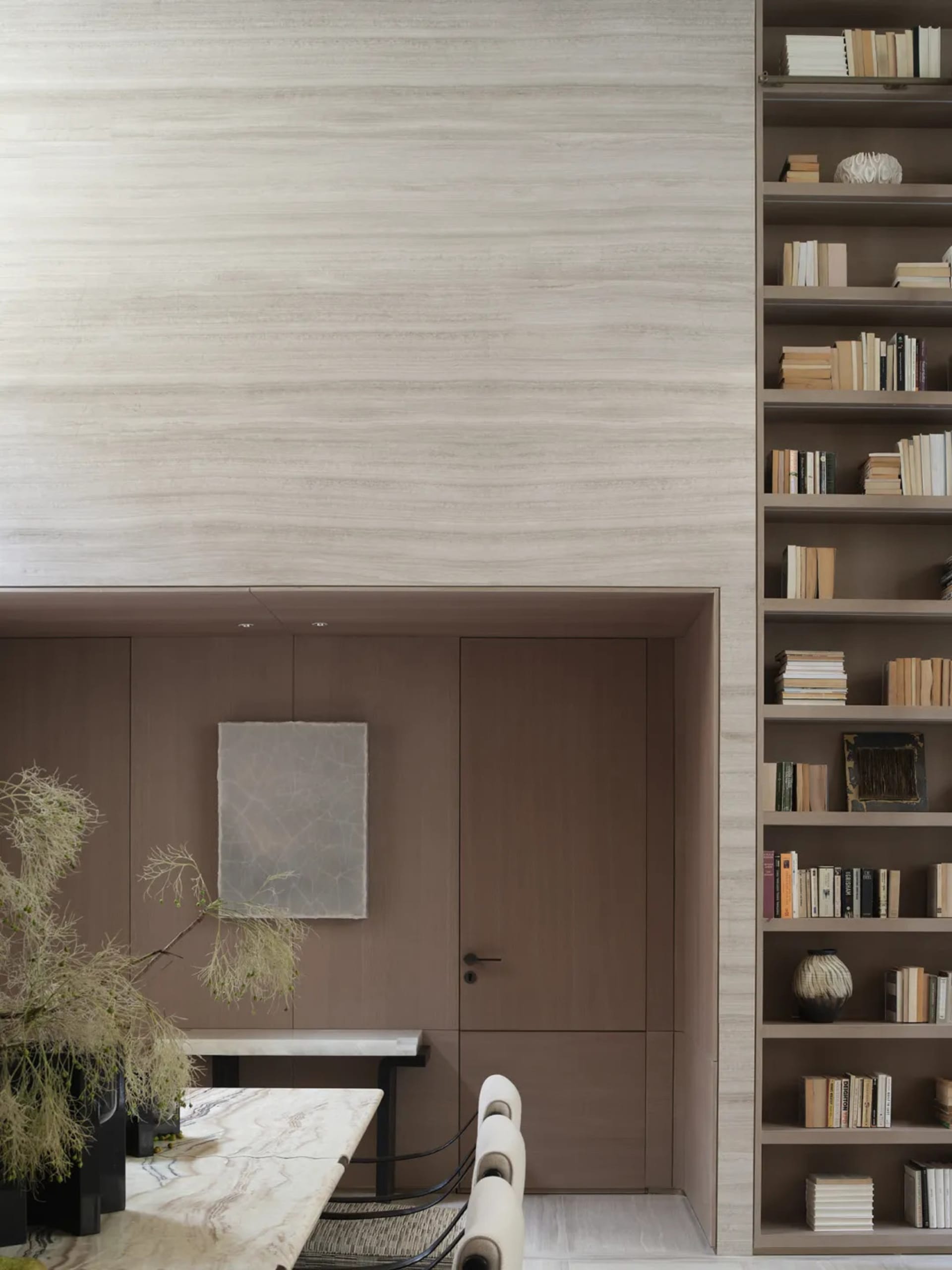 A modern minimalist library with wooden walls and shelves filled with books, featuring a minimalist door and a wooden table.