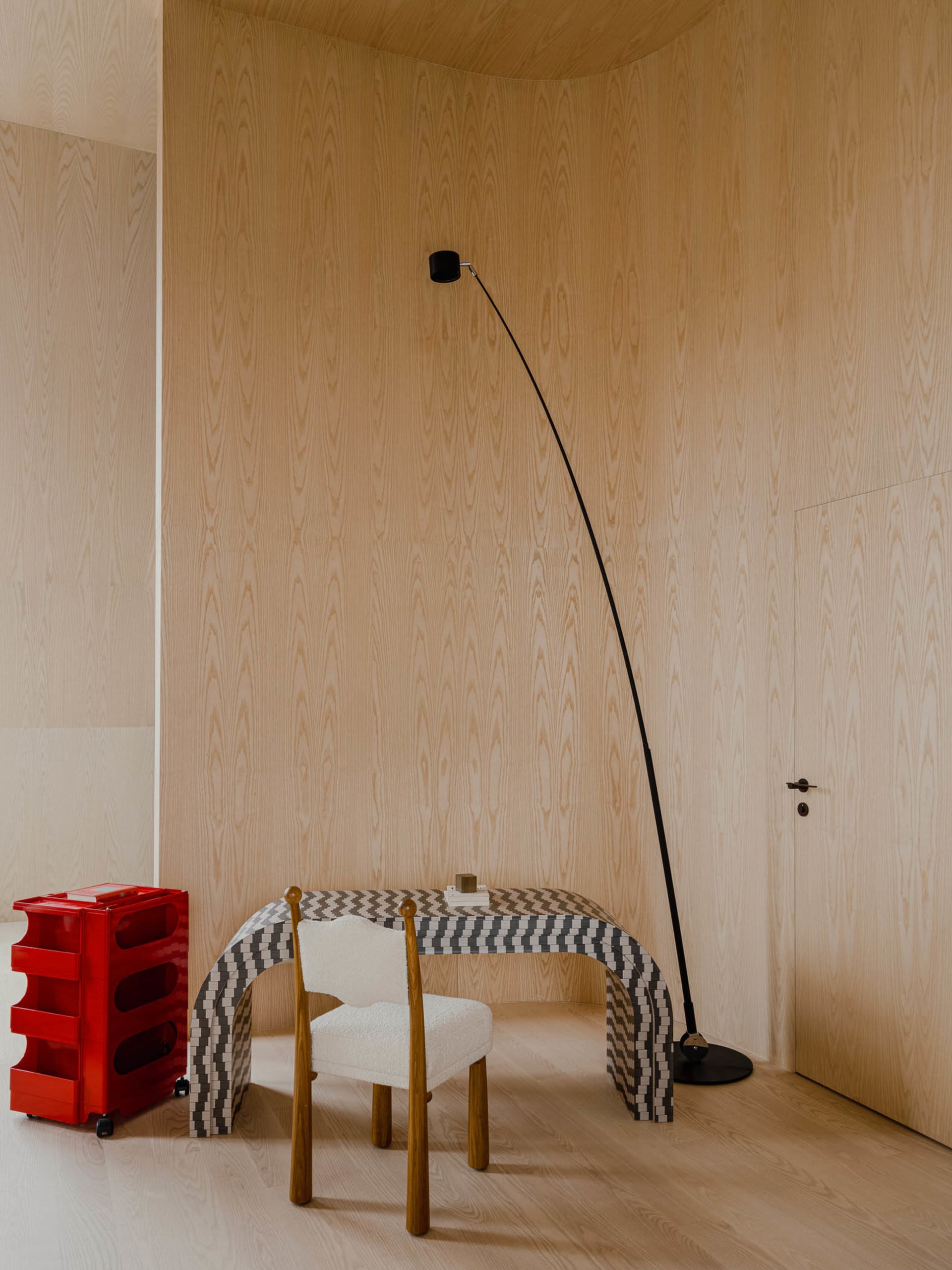 A modern workstation with a unique curved desk, a white upholstered chair, and a red rolling cart with transparent drawers in