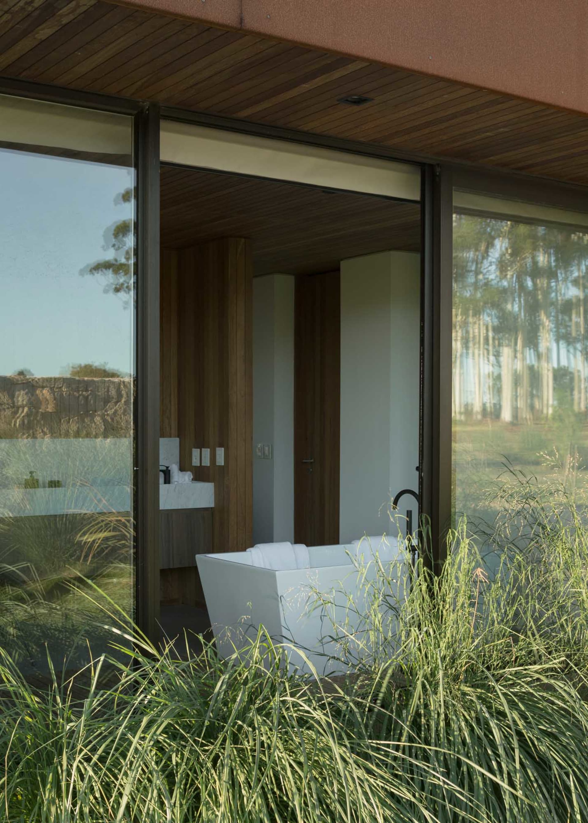 Minimalist bathroom with concrete walls and white freestanding bathtub surrounded by green plants.