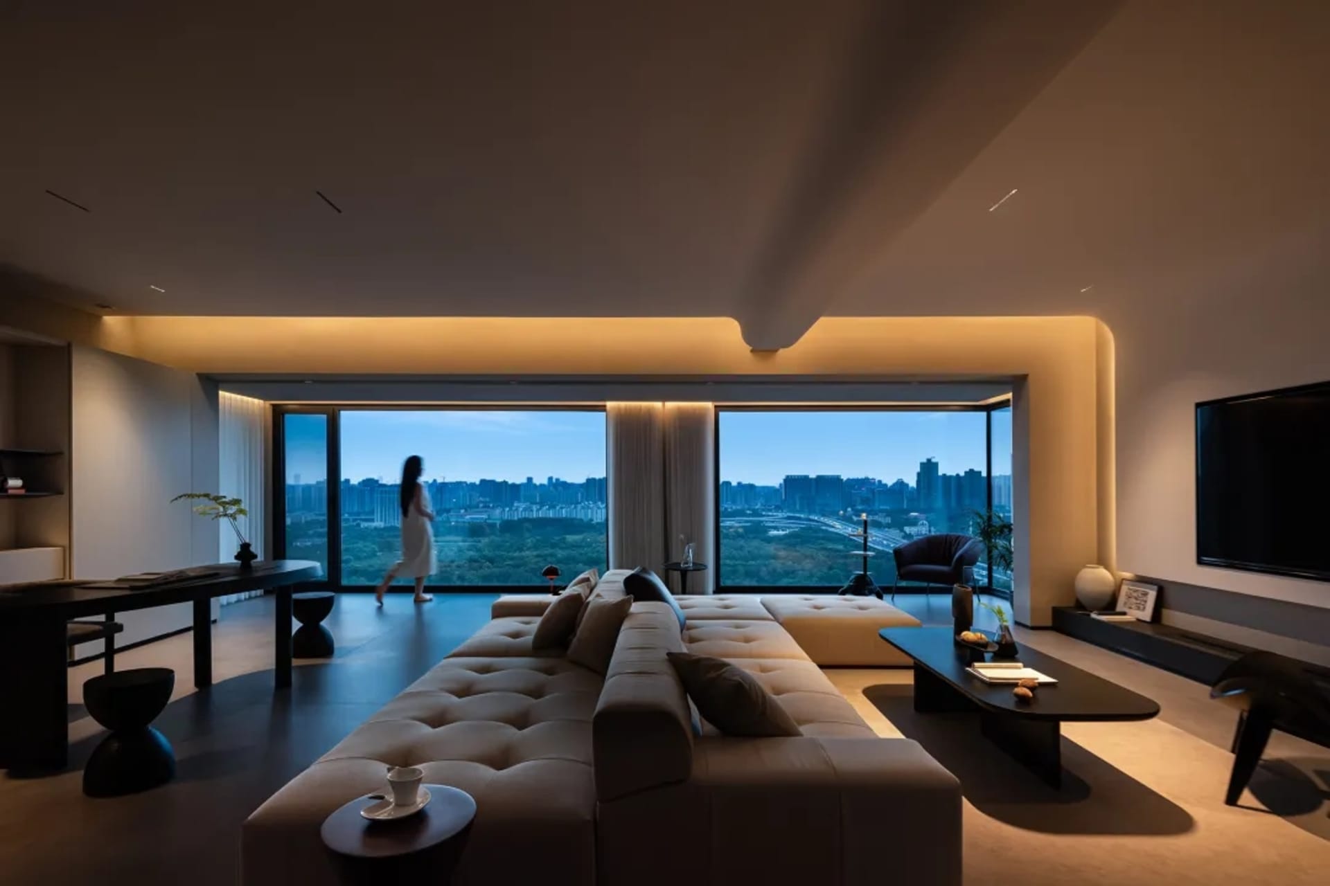 A modern apartment living room featuring minimalist furniture and large windows overlooking a cityscape.