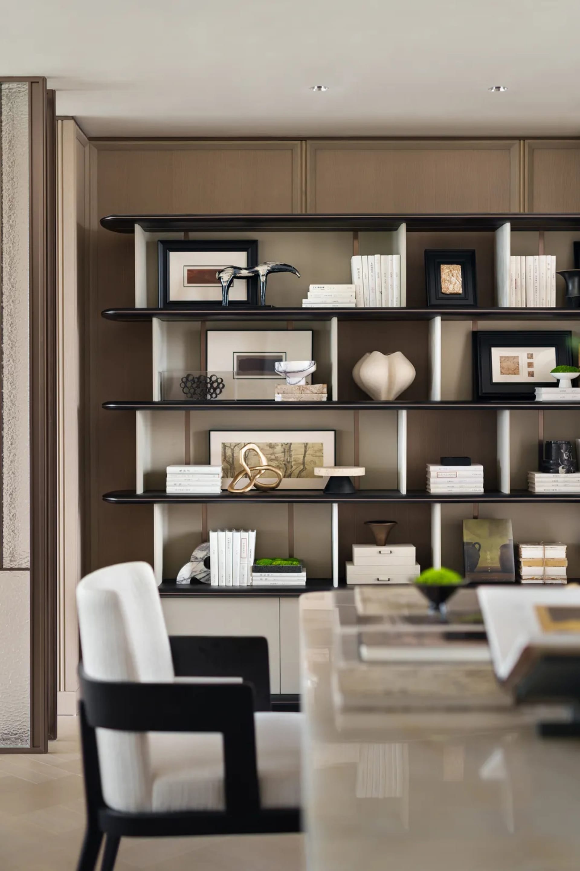 A modern, minimalist library interior featuring a shelf with books, frames, and decorative objects.