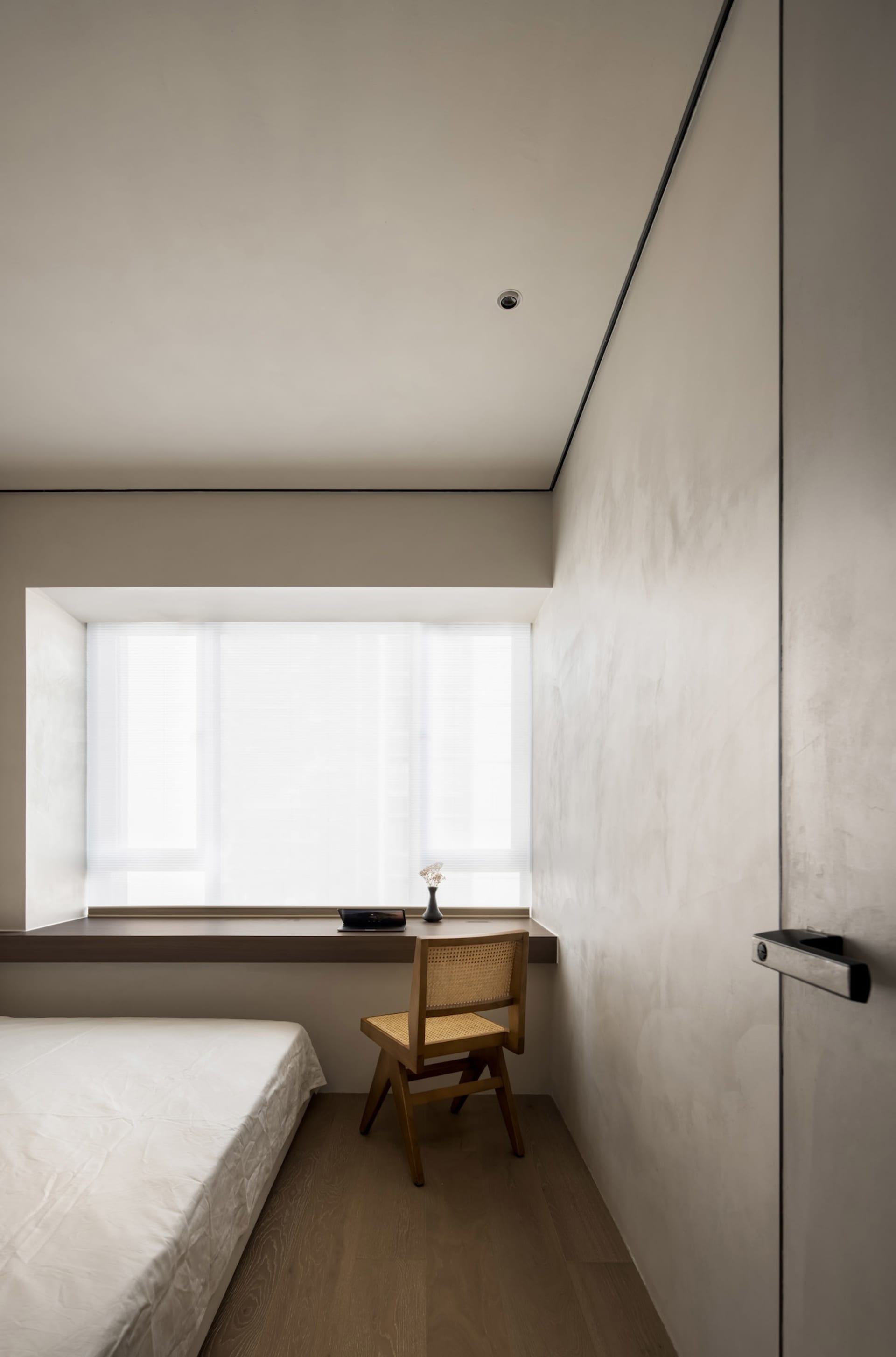 A minimalist bedroom with a bed, chair, and window.