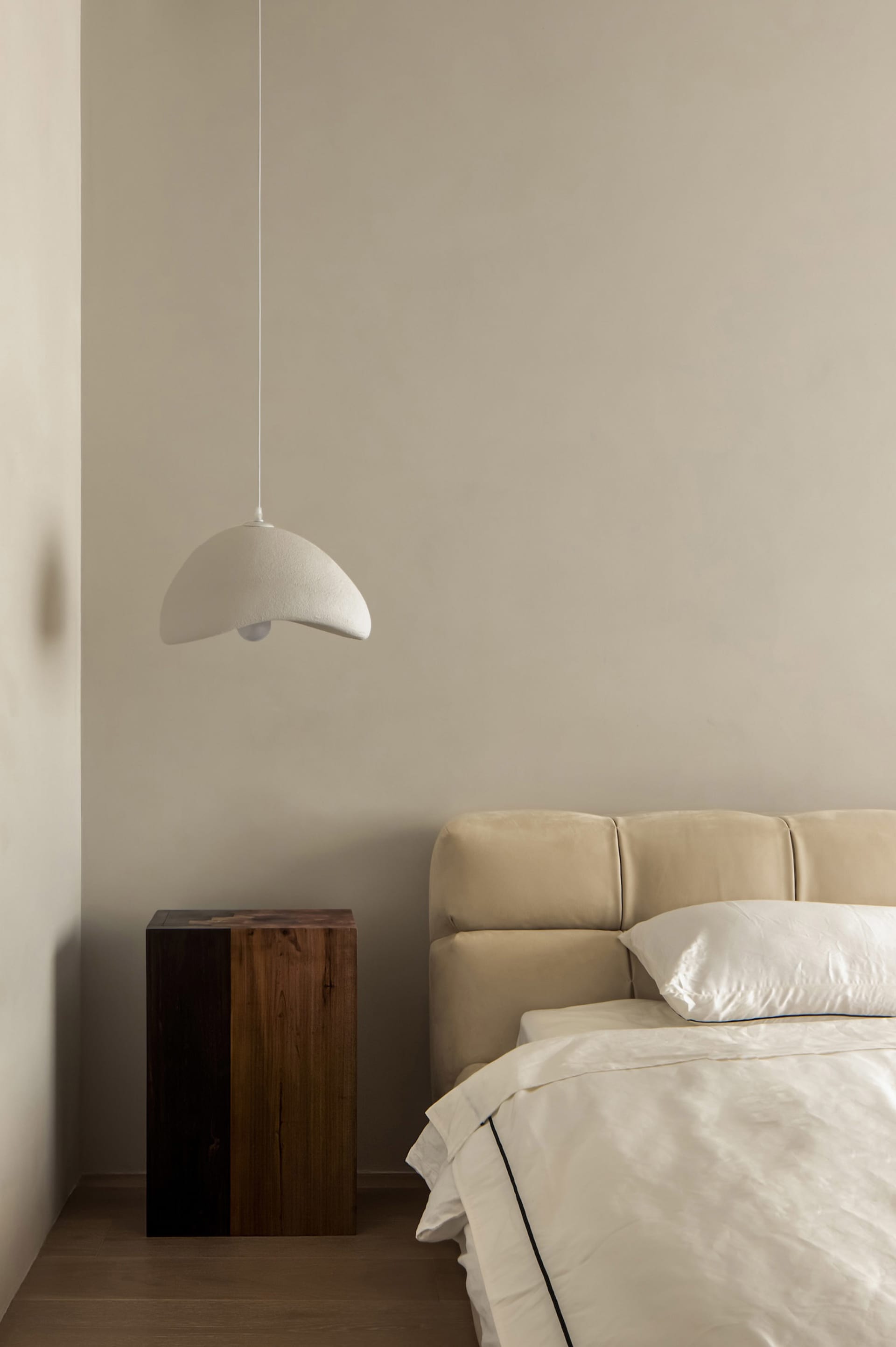 A minimalist bedroom featuring a textured lamp hanging above the bed.