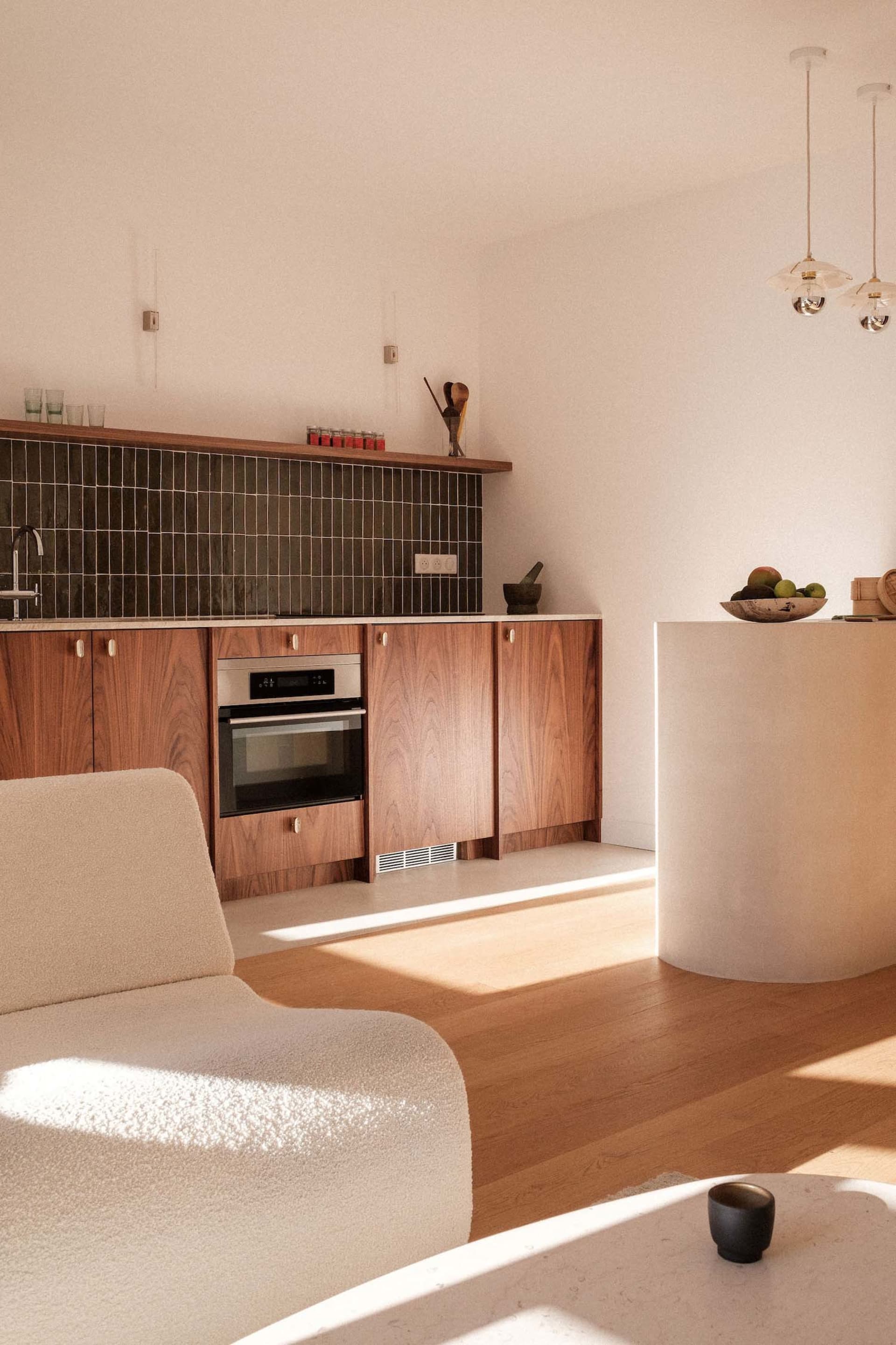 Modern kitchen with light wood cabinets, dark tile backsplash, and white countertops.