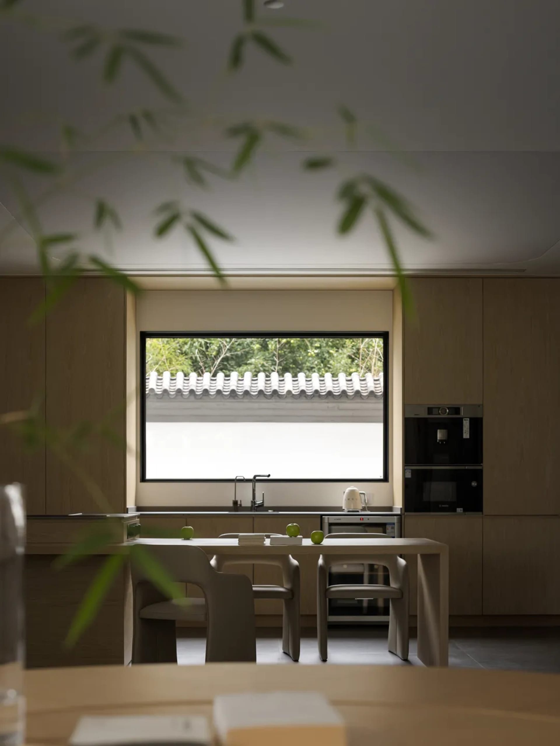 現代廚房擁有木質櫥櫃、餐桌與餐椅，置於大型窗戶下，可眺望綠意盎然的景觀。