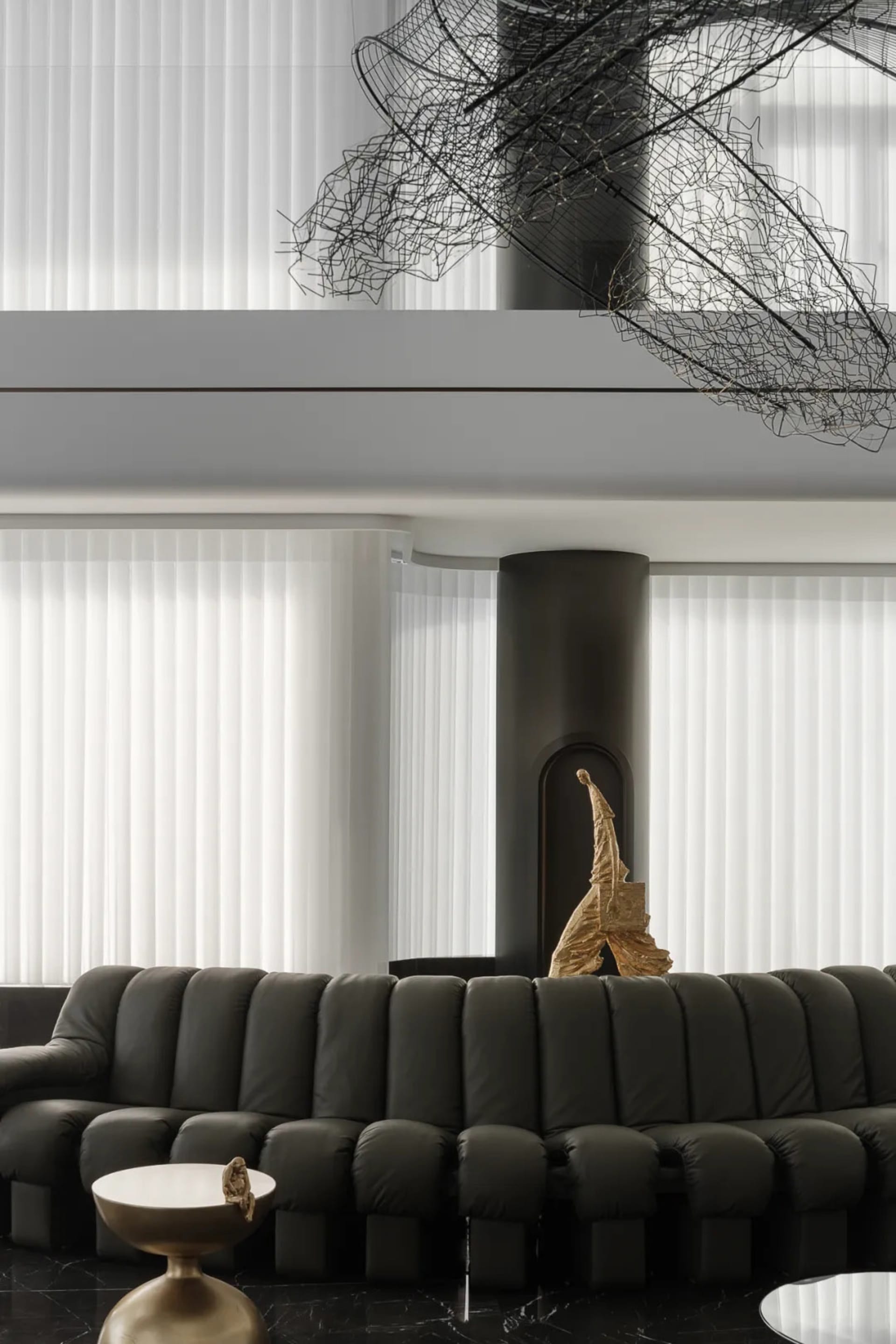 A modern living room featuring a black leather sofa, a sleek side table with a golden statue, and large windows with white bl