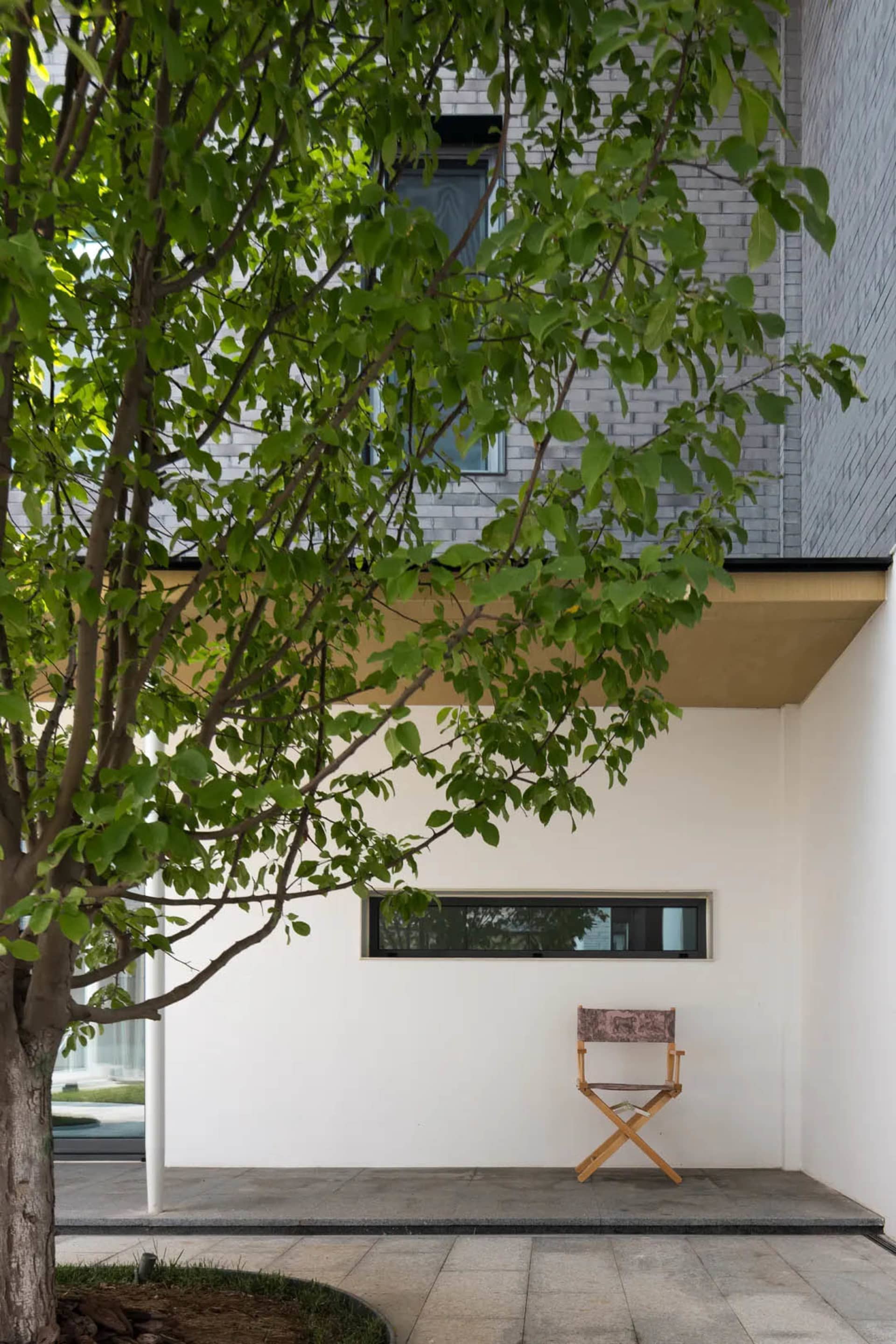 A minimalist modern building exterior made of concrete, featuring a tree and a director's chair.