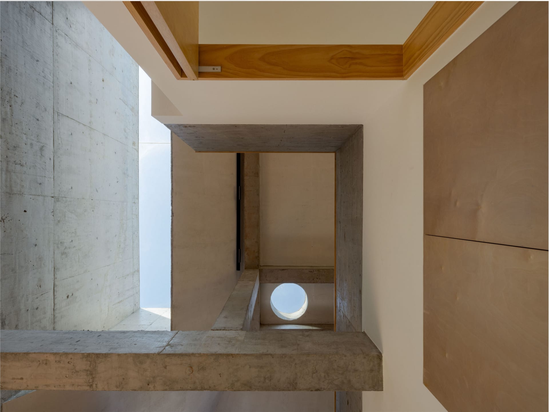 Modern interior with concrete walls and wooden accents, featuring a circular skylight and natural light.