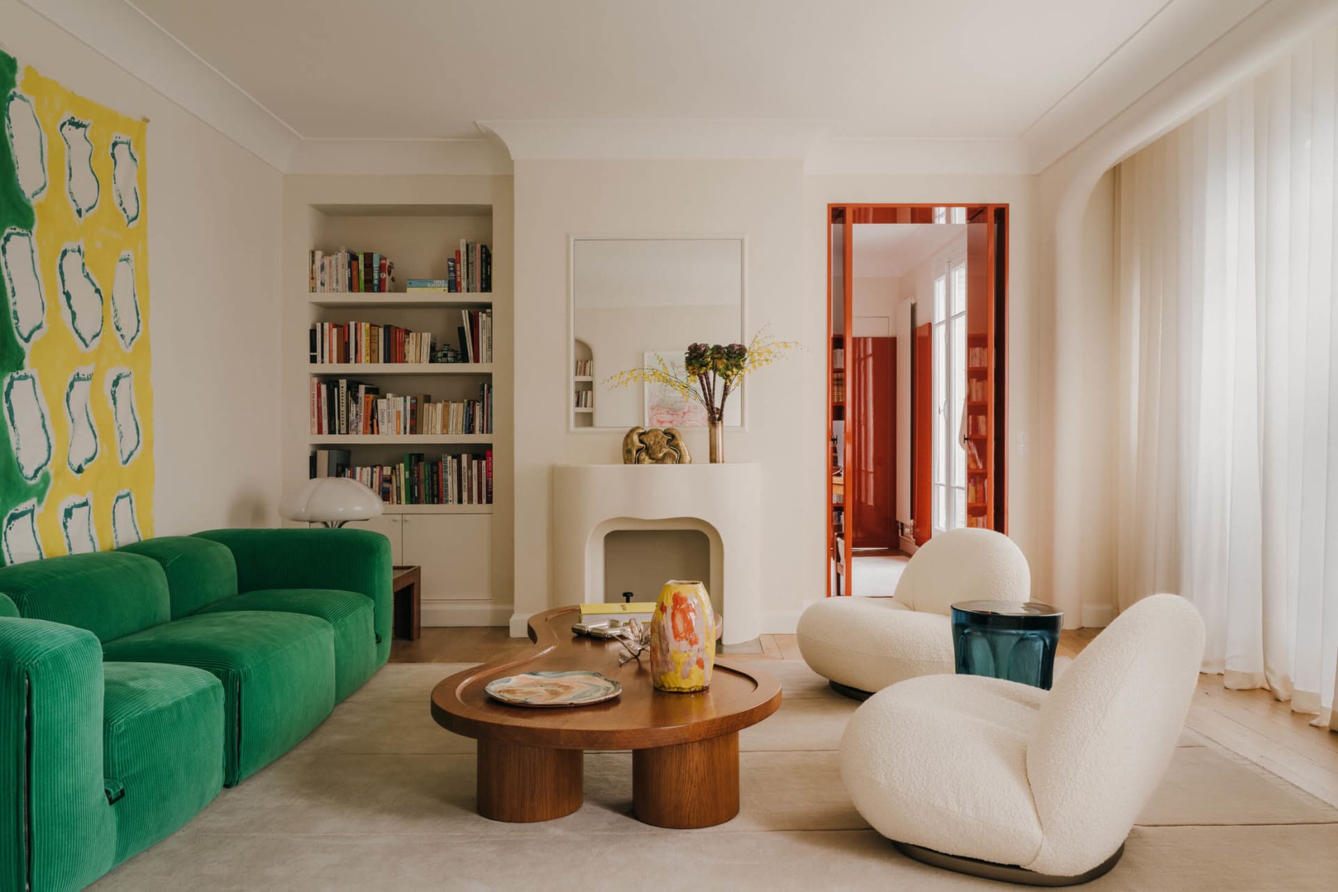 A modern living room featuring a green sofa with white cushions, wooden coffee table, and bookshelf.
