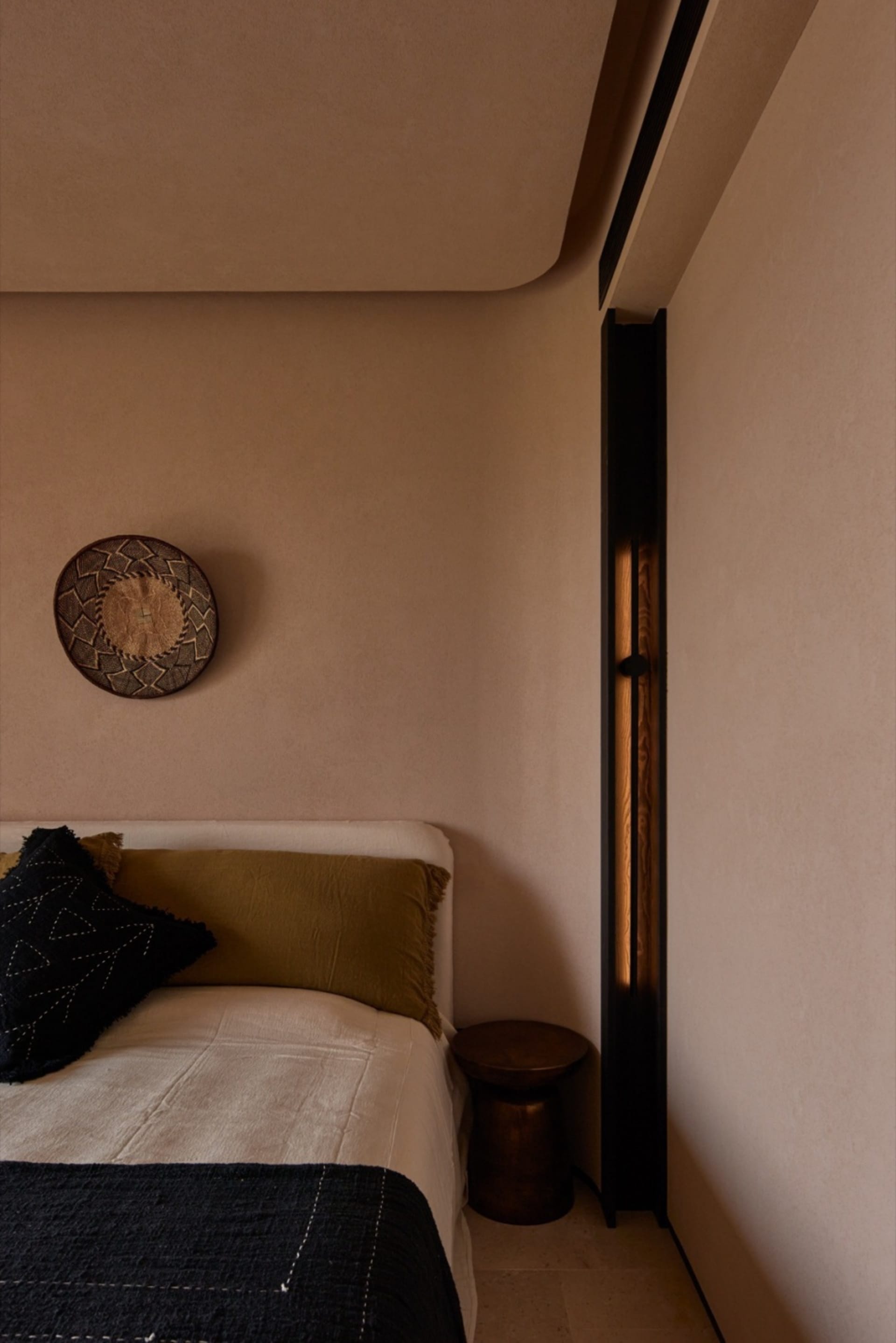 Minimalist bedroom with a bed, bedside stool, and decorative basket on the wall.